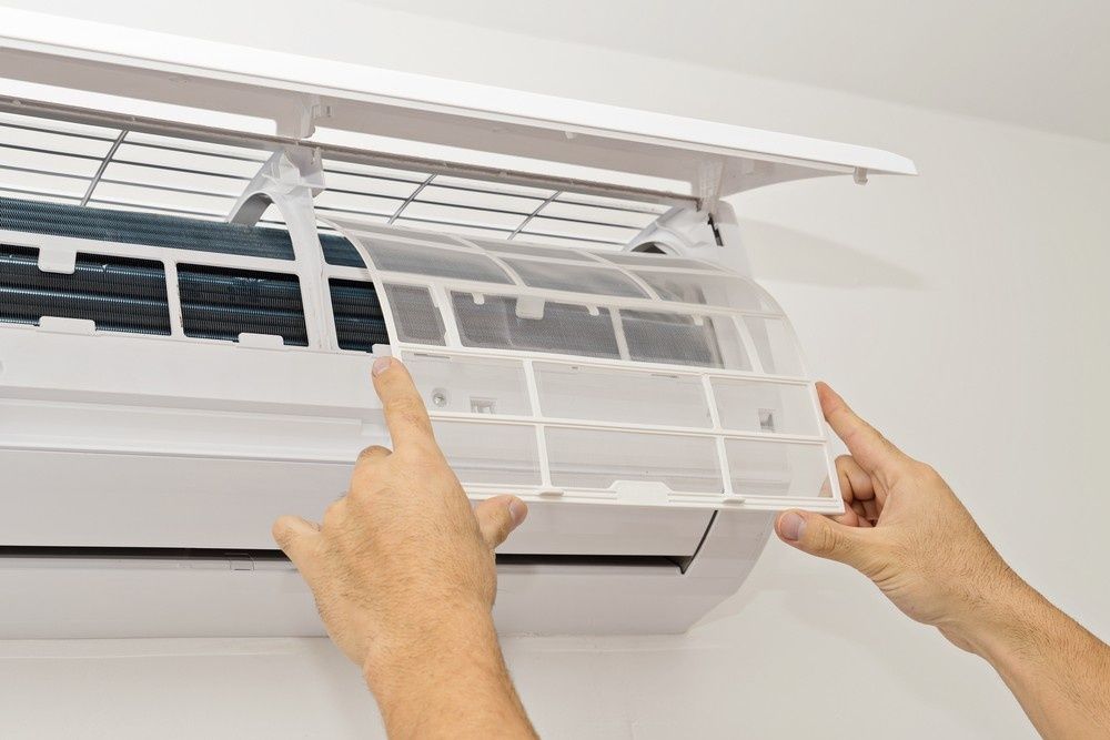 Person Removing an Air Filter from A Wall-Mounted Air Conditioner — Messina Air Conditioning & Electrical in Kuranda, QLD