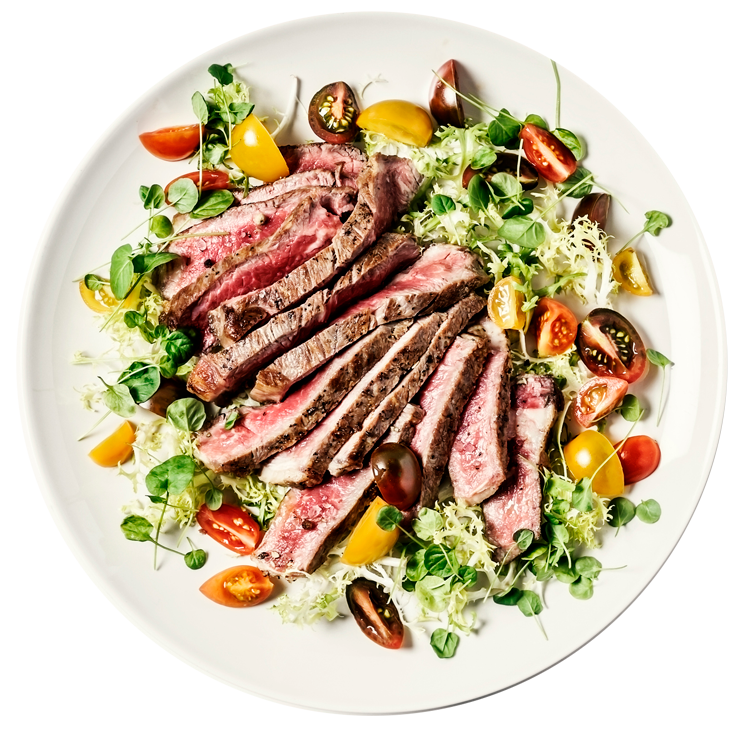 A white plate topped with sliced steak and vegetables.