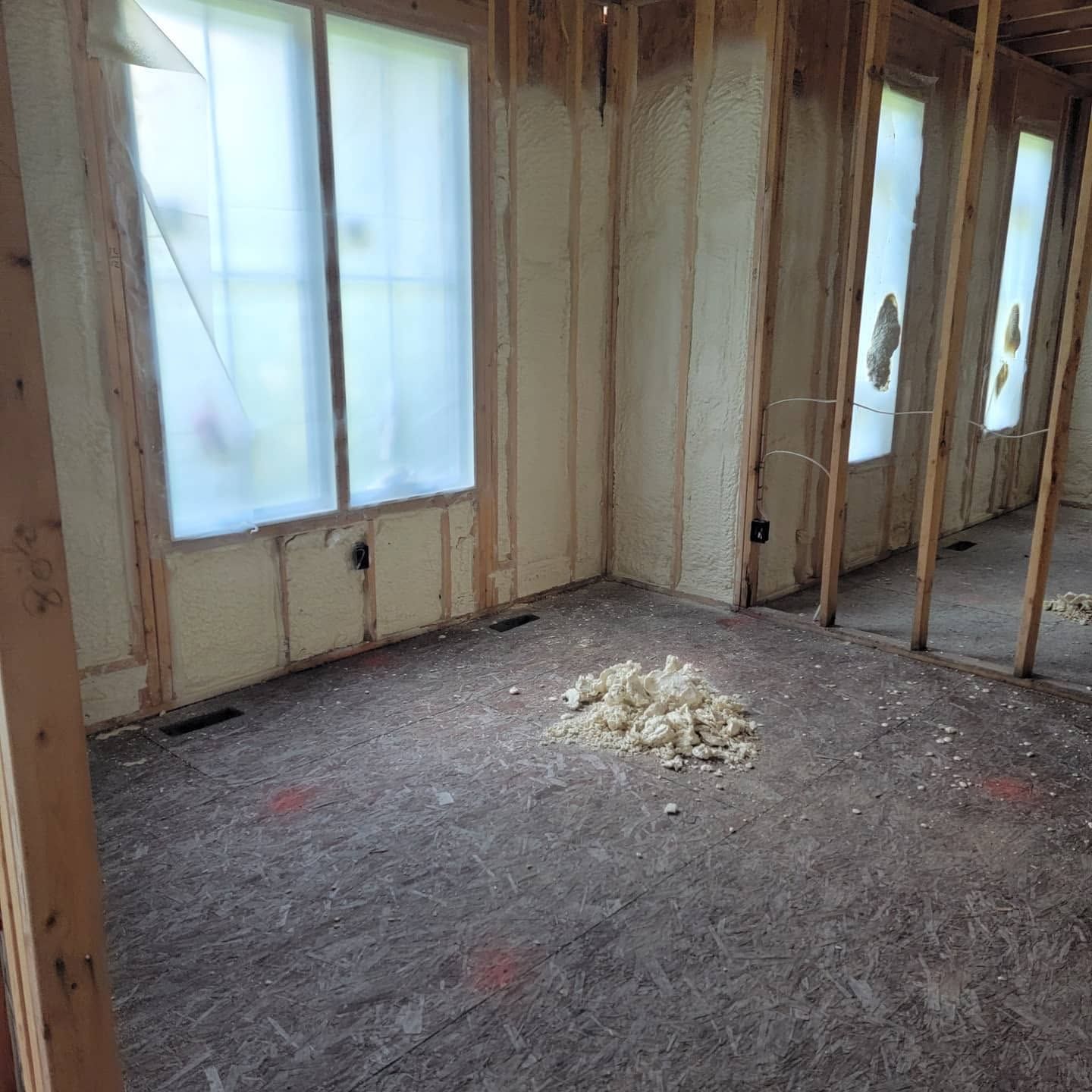 Partially insulated room under renovation with exposed framing, windows, and debris on the floor