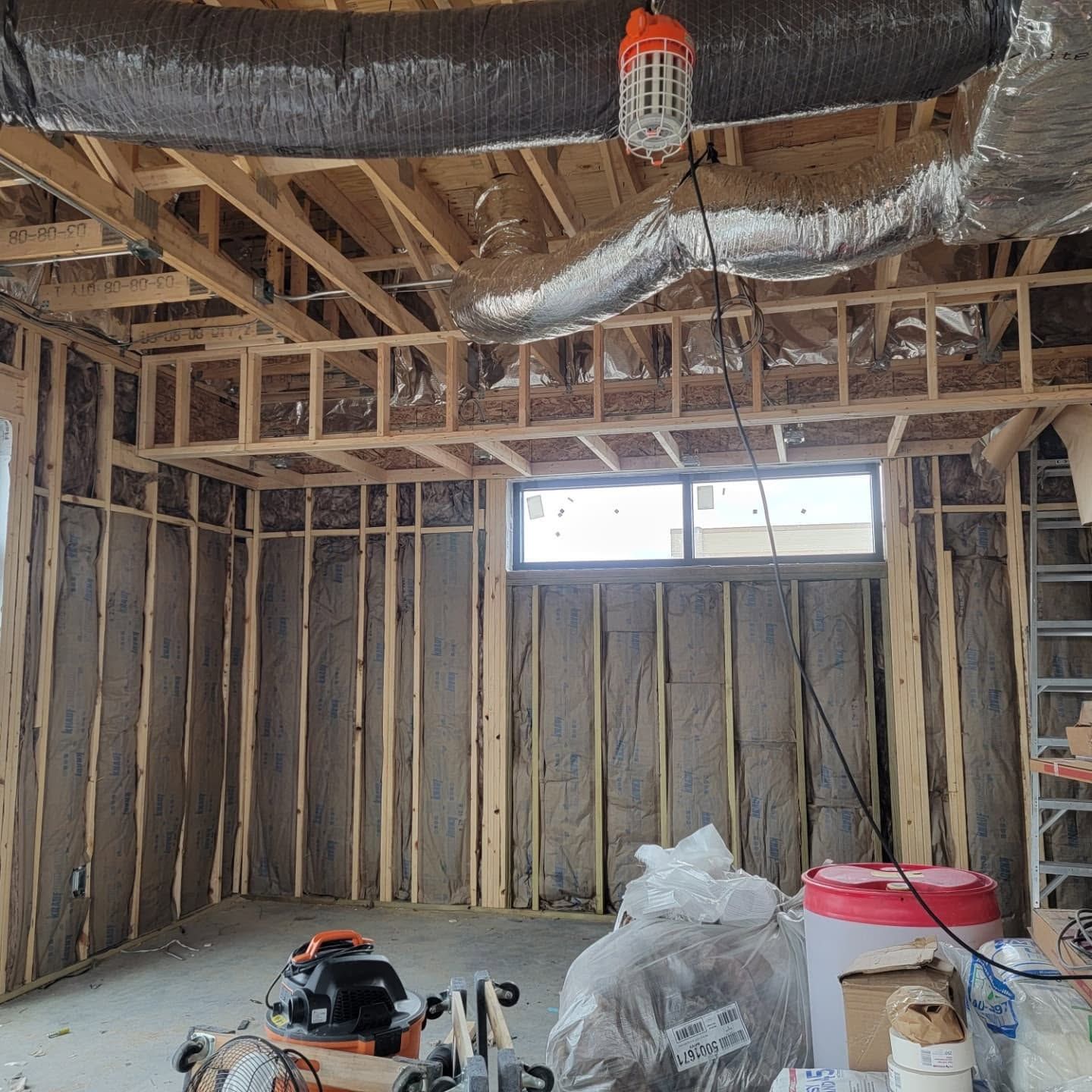 Unfinished room with exposed wood framing, insulation ducts, a window, and construction tools on the floor.