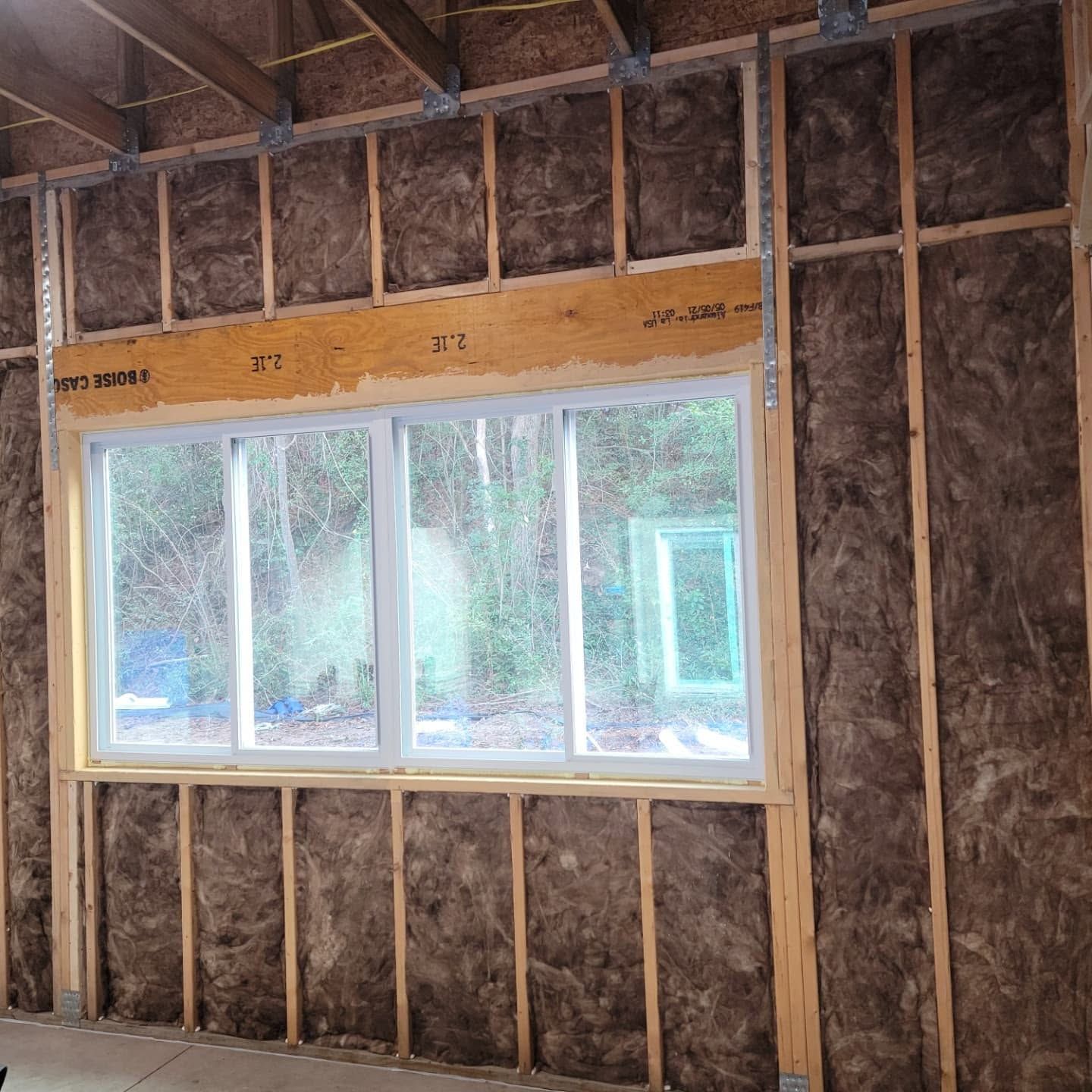 Unfinished interior wall framing with insulation and a framed window letting in daylight