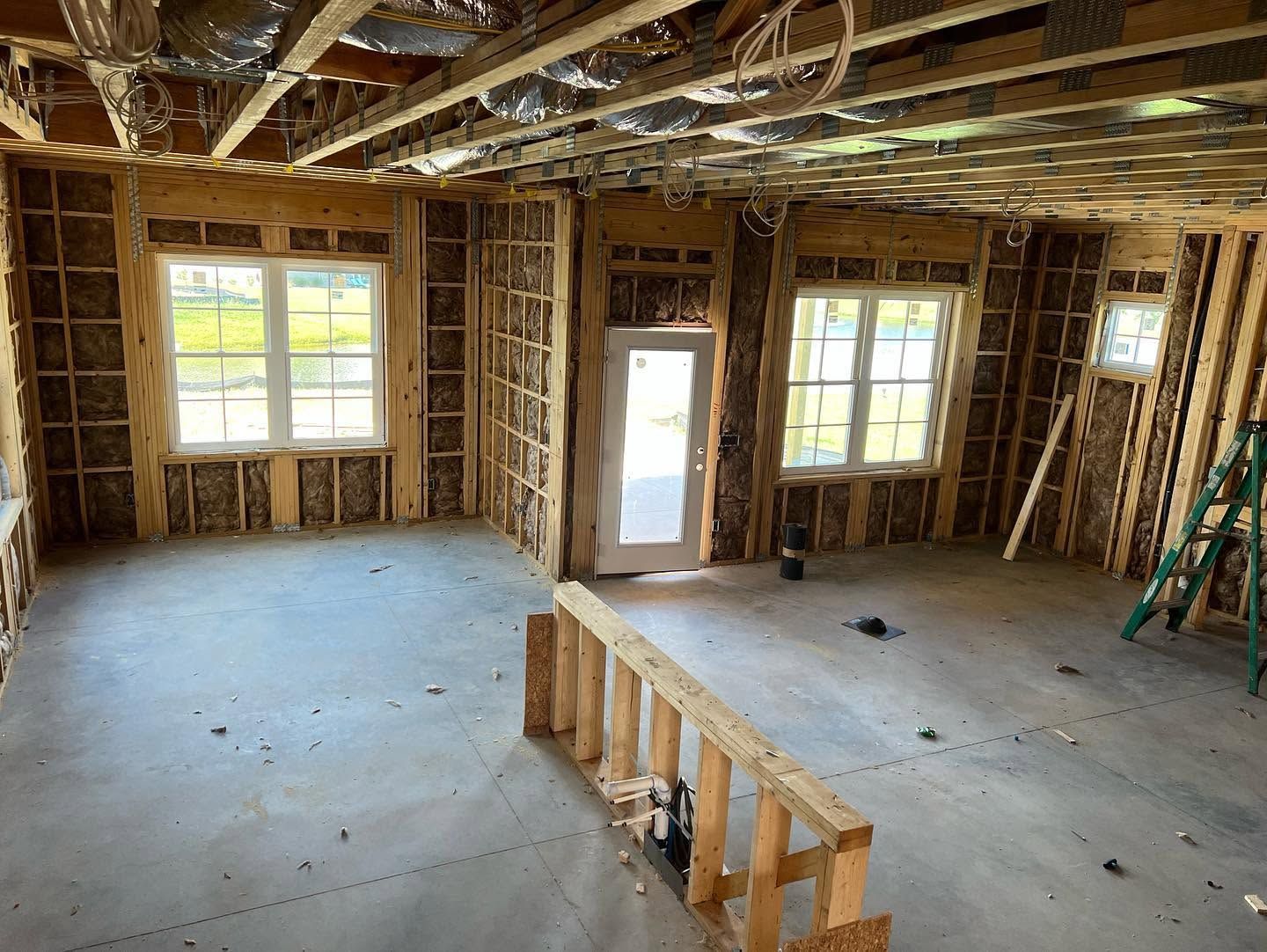 Unfinished room with exposed framing, bare subfloor, windows, and a partial staircase opening.