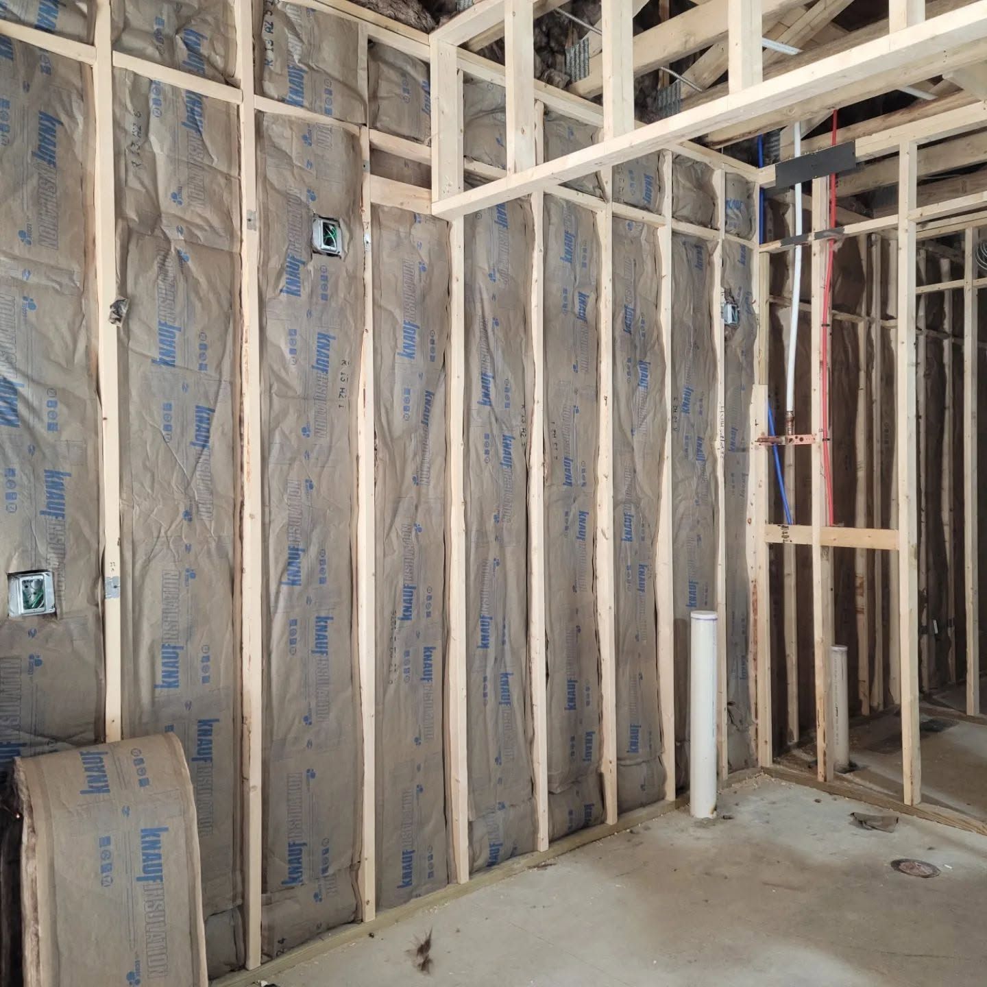 Unfinished interior wall framing with insulation, exposed studs, and a concrete floor.