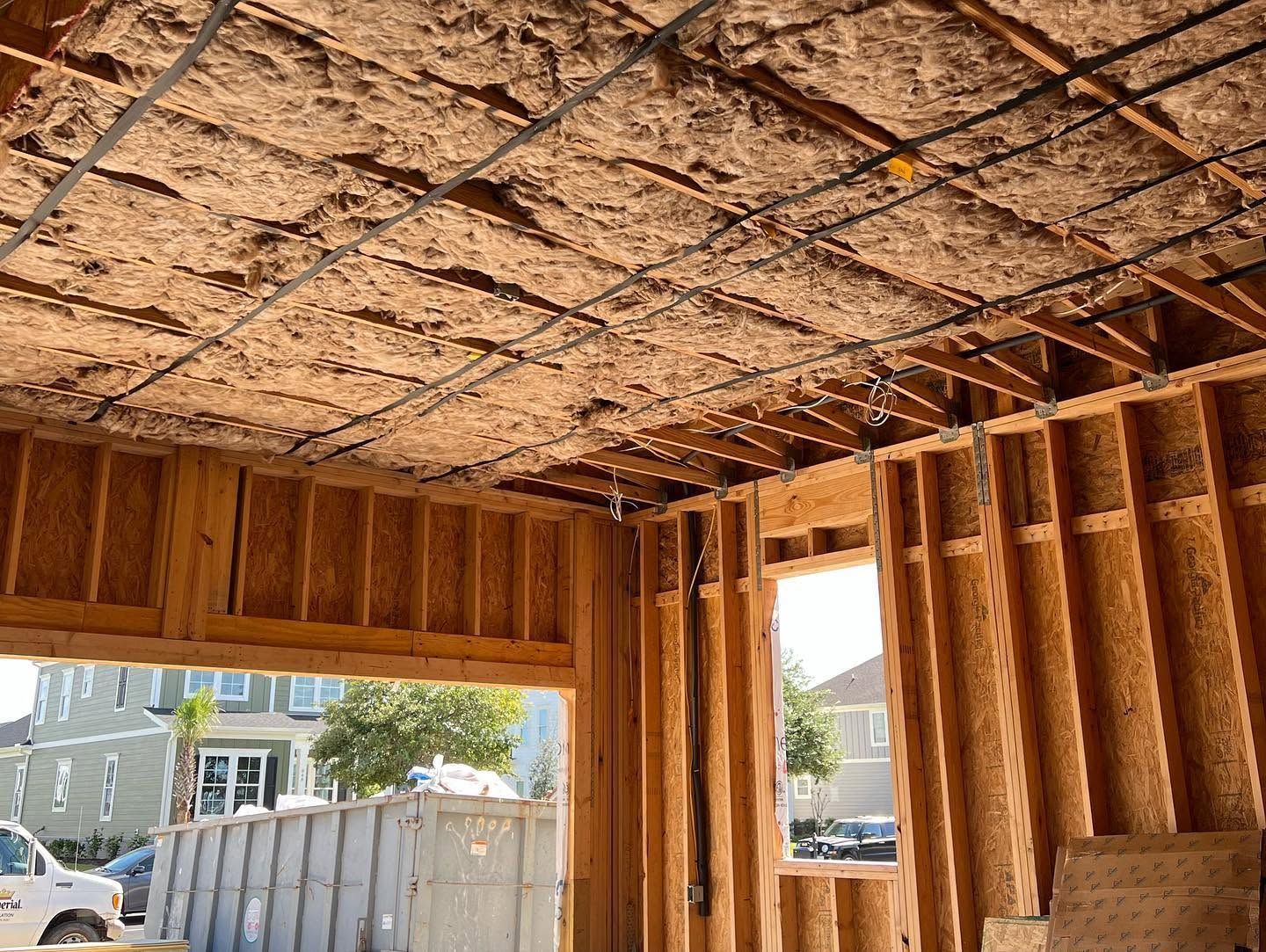 Interior of a wooden-framed room under construction, with exposed ceiling insulation and open window bays