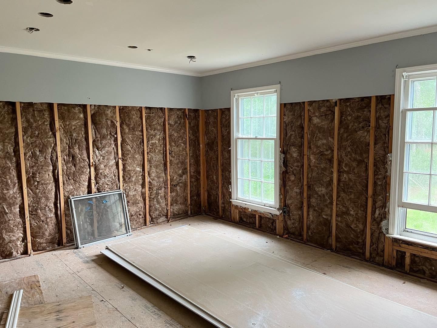 Empty room under renovation with exposed insulation and unfinished drywall on floor