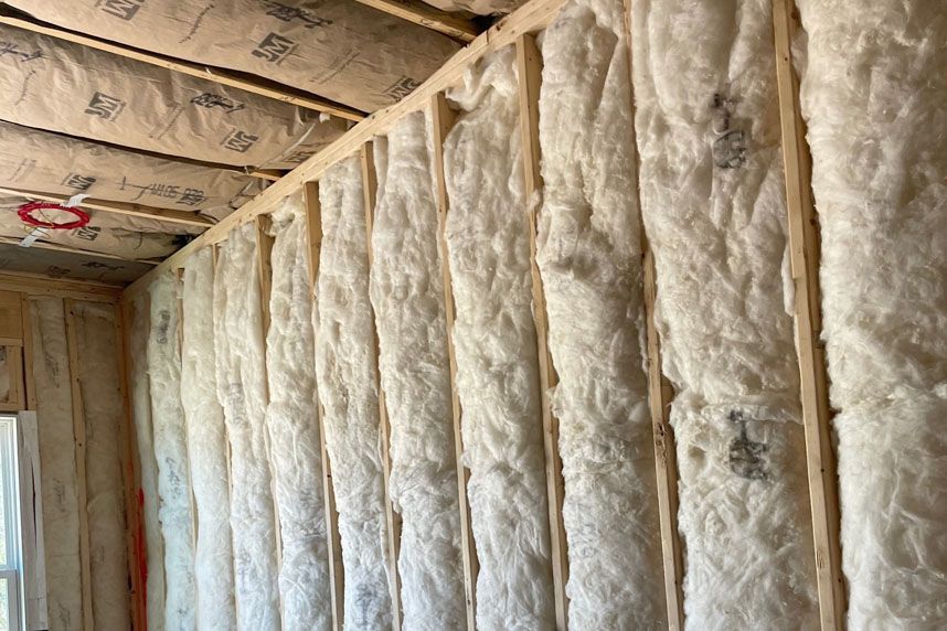 Interior wall with exposed wooden studs and white insulation batts in an unfinished room