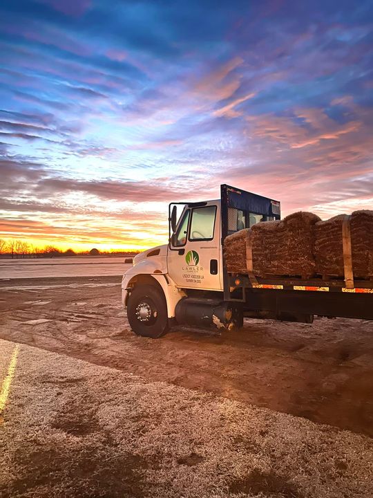 White truck loaded with objects on a dirt road at sunset; orange and blue sky.