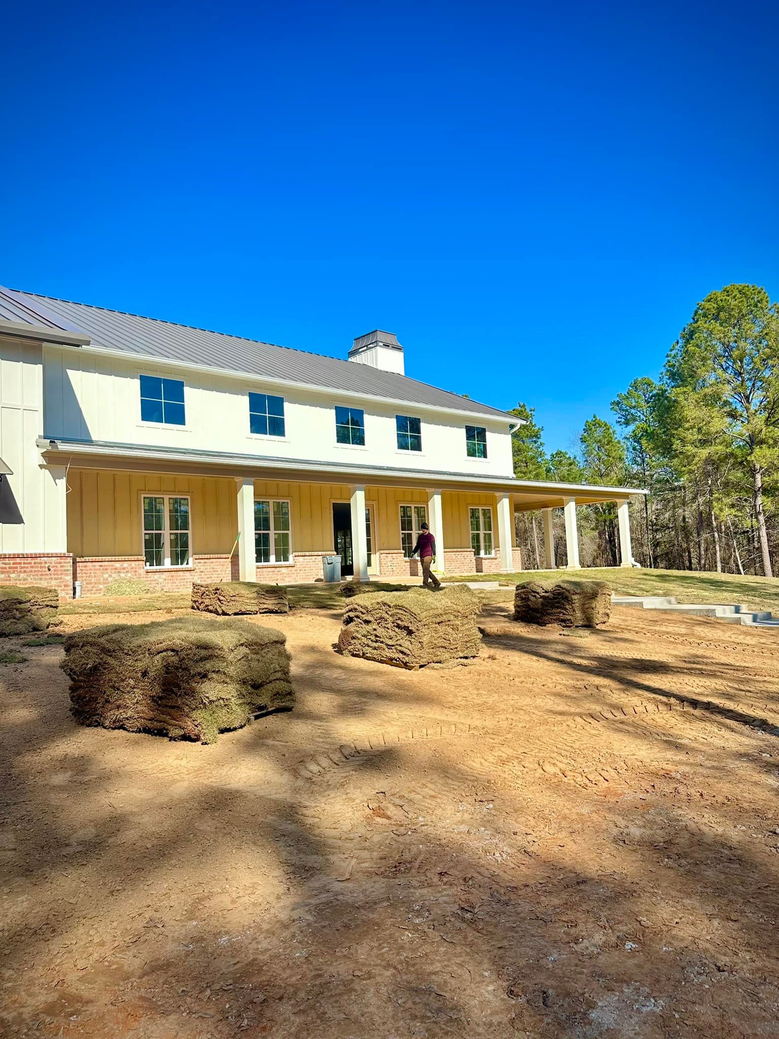 Two-story yellow house with a covered porch. Three soil blocks in the foreground. Blue sky.