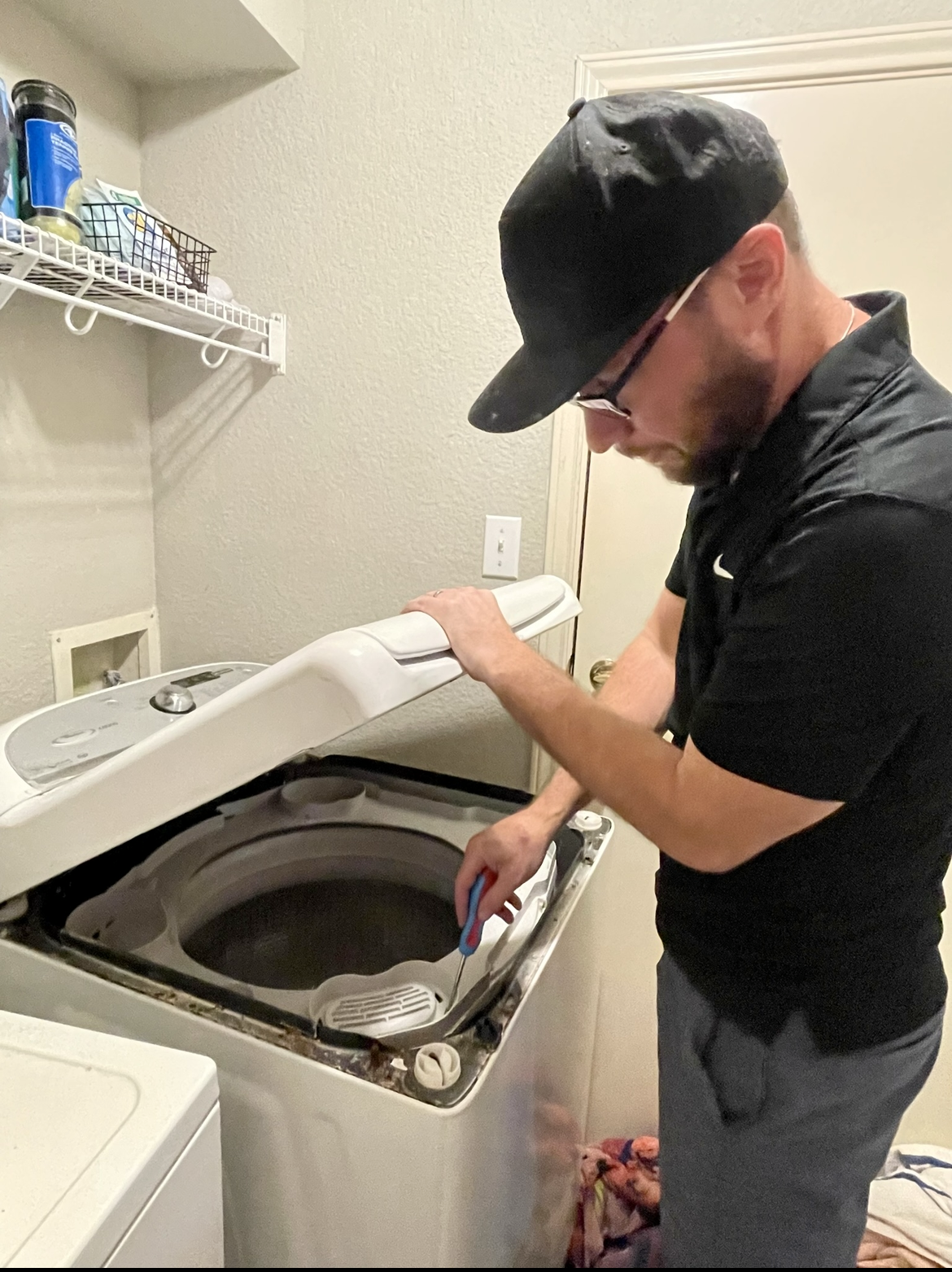 Man cleaning the interior of a top-loading washing machine in a laundry room