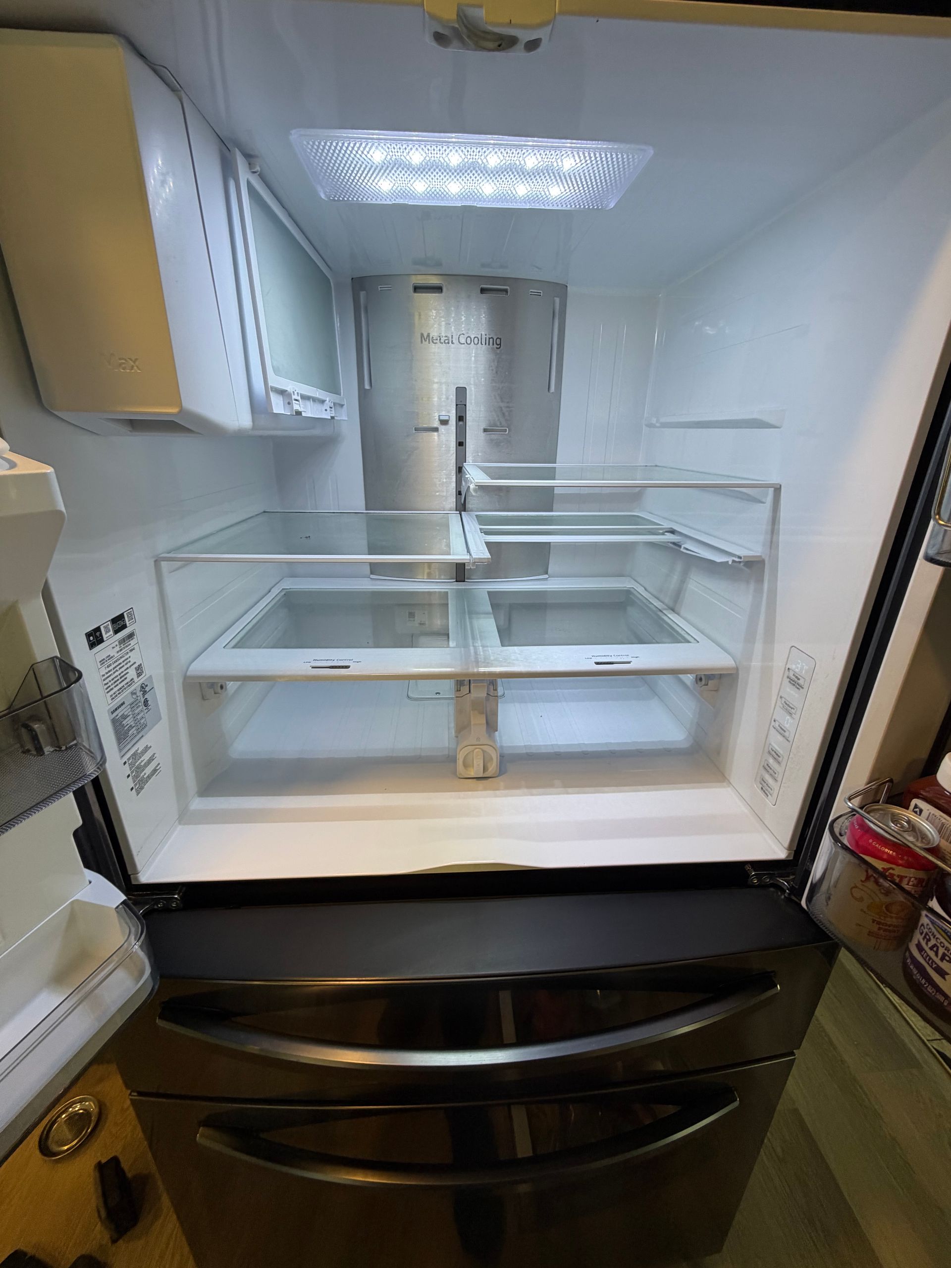 Open refrigerator with empty shelves and drawers lit by a top light