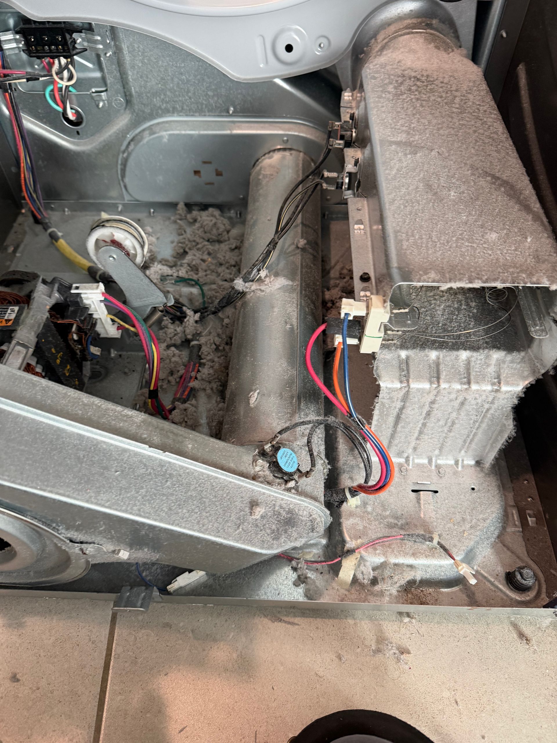 Dusty vehicle interior with exposed wiring, metal panels, and a cylindrical component.