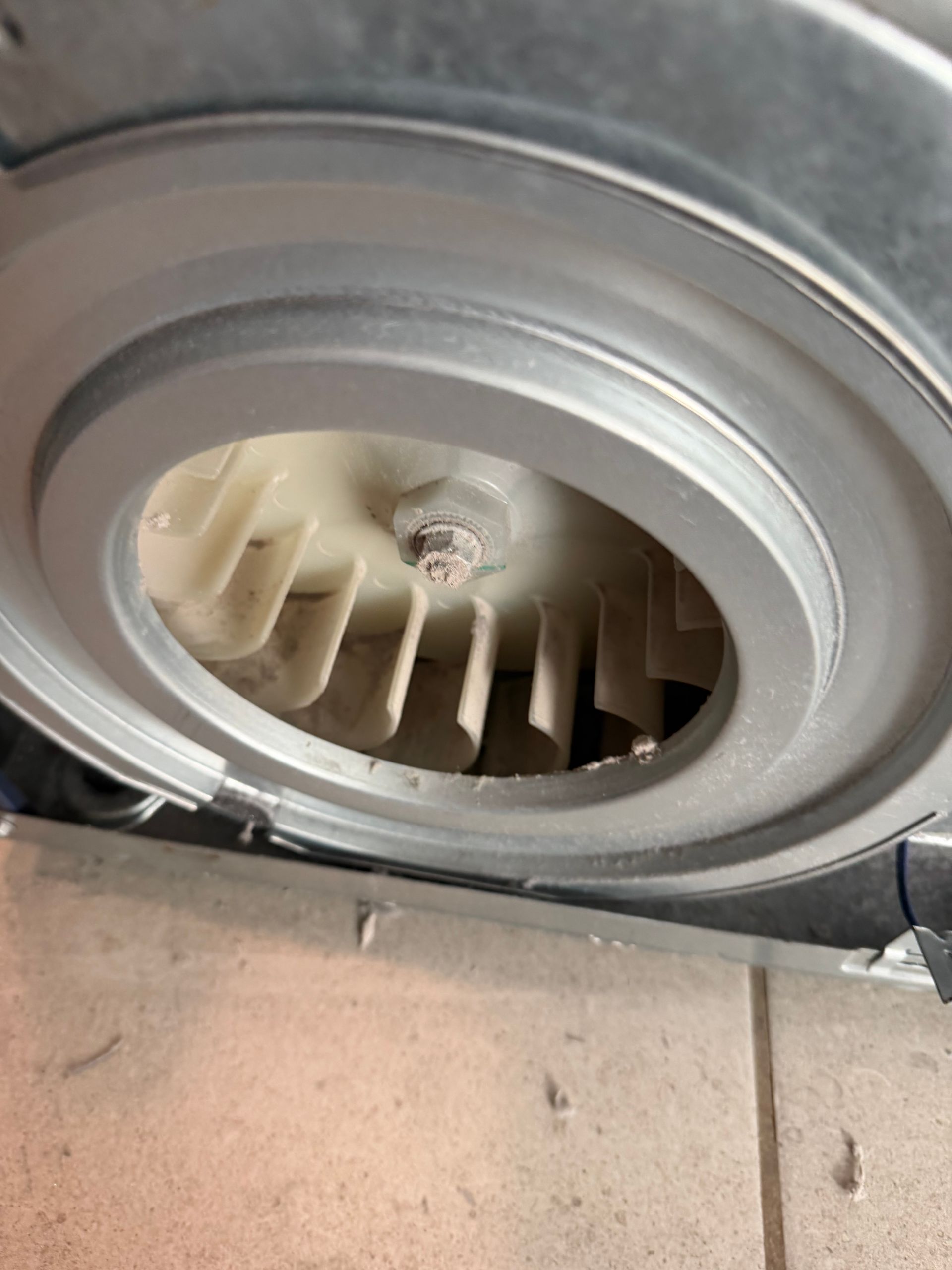 Close-up of a circular metal vent or turbine fan with beige blades inside a silver frame.