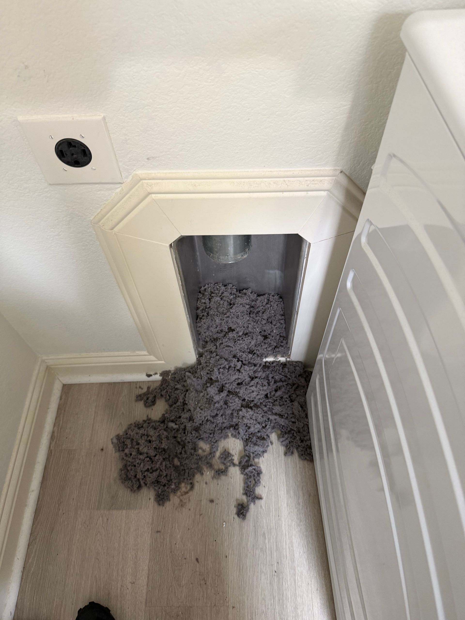 Gray pellets spilling from a wall pet door onto a carpeted floor beside a white cabinet