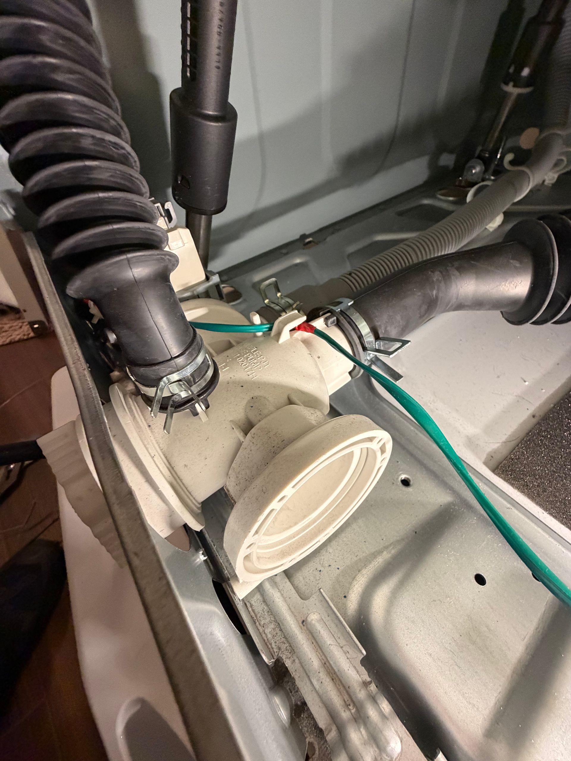 Close-up of appliance wiring and hoses inside a machine compartment with a beige plastic component.