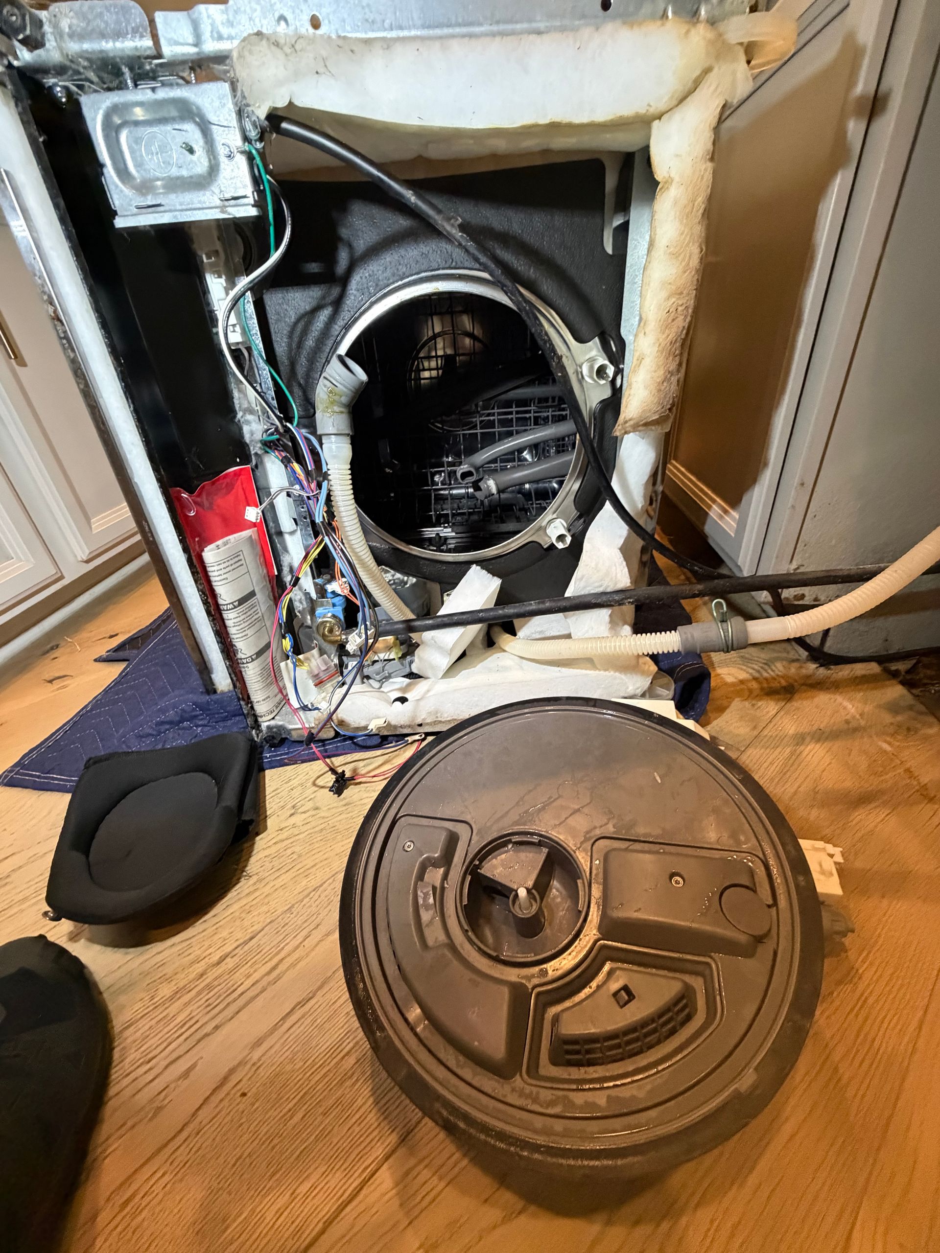 Open dryer with front panel removed, exposing wiring and drum, repair parts on the floor nearby