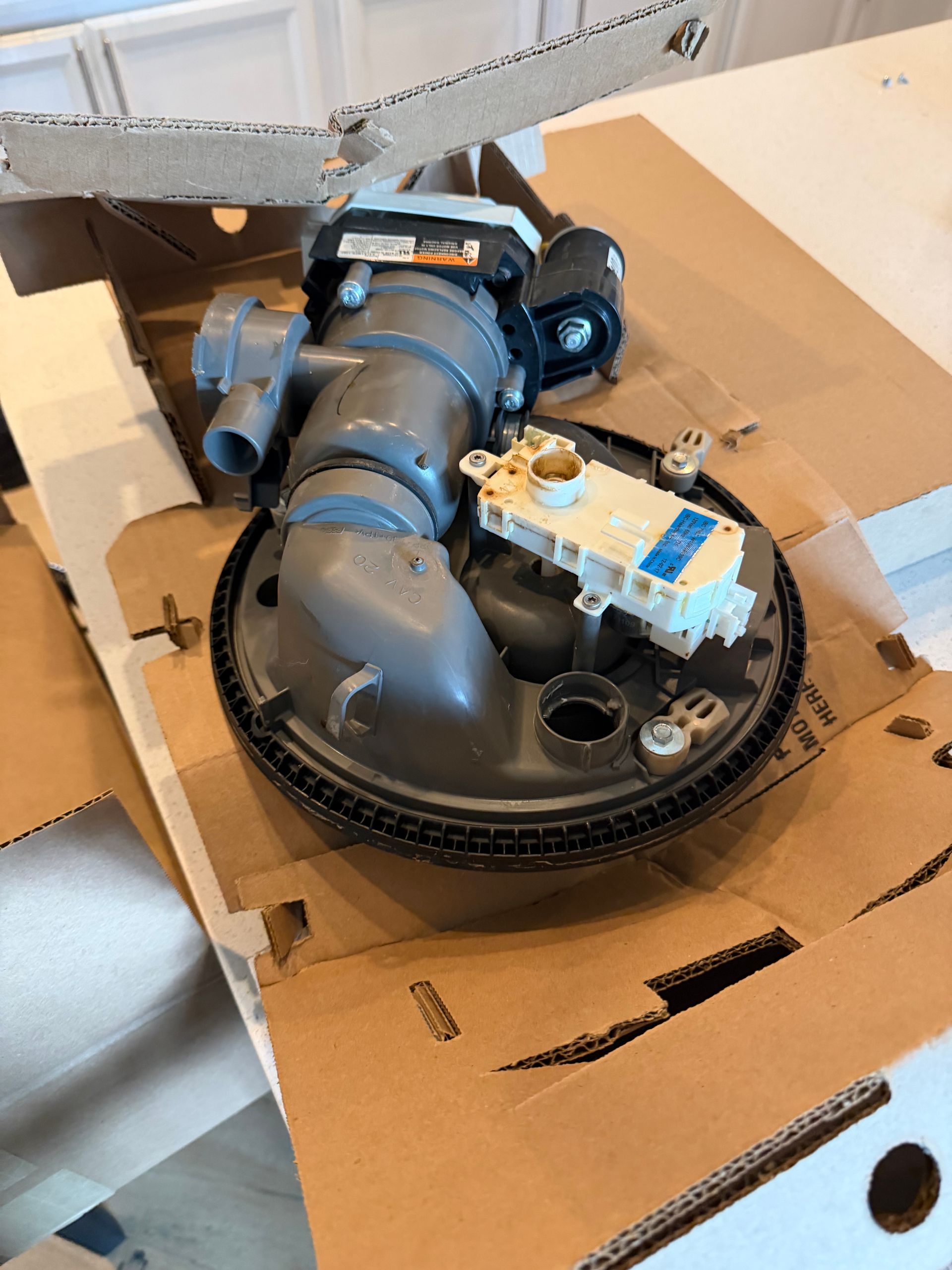 Blue robotic vacuum parts inside a torn cardboard box on the floor