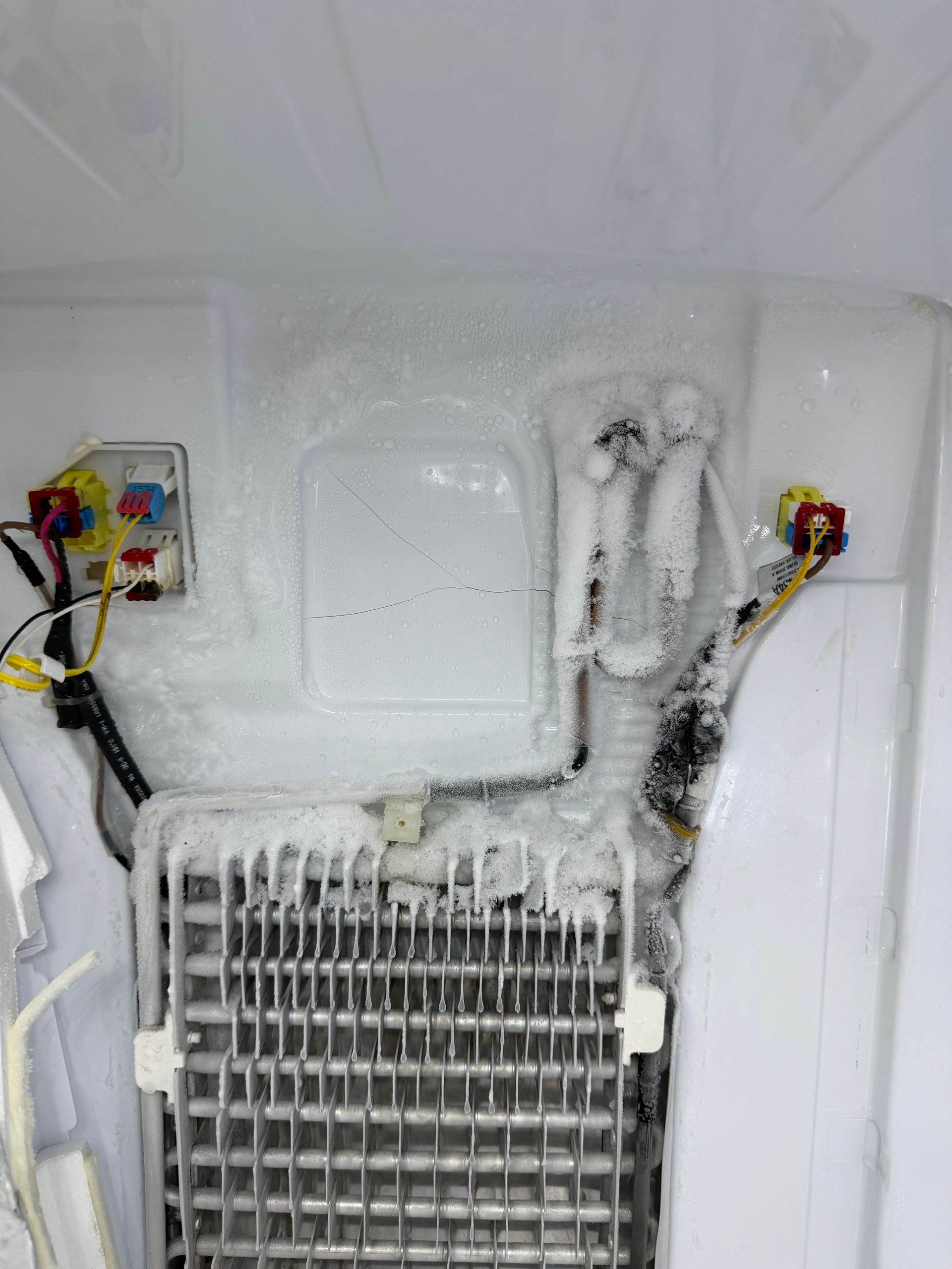 Ice-covered refrigerator freezer interior with frosted coils and wiring exposed above the vent.