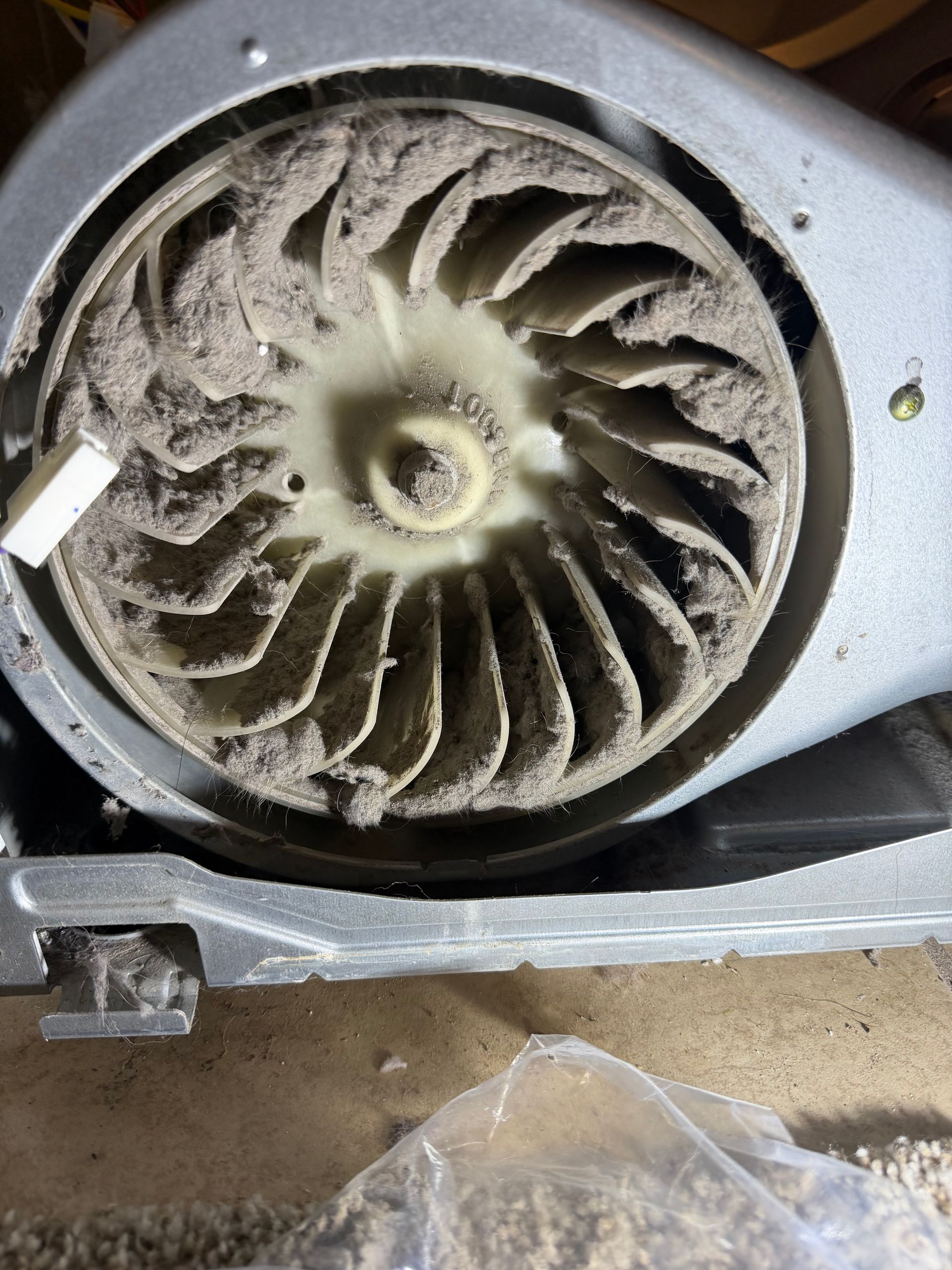 Dust-covered circular blower fan inside a metal housing, viewed close up with debris below