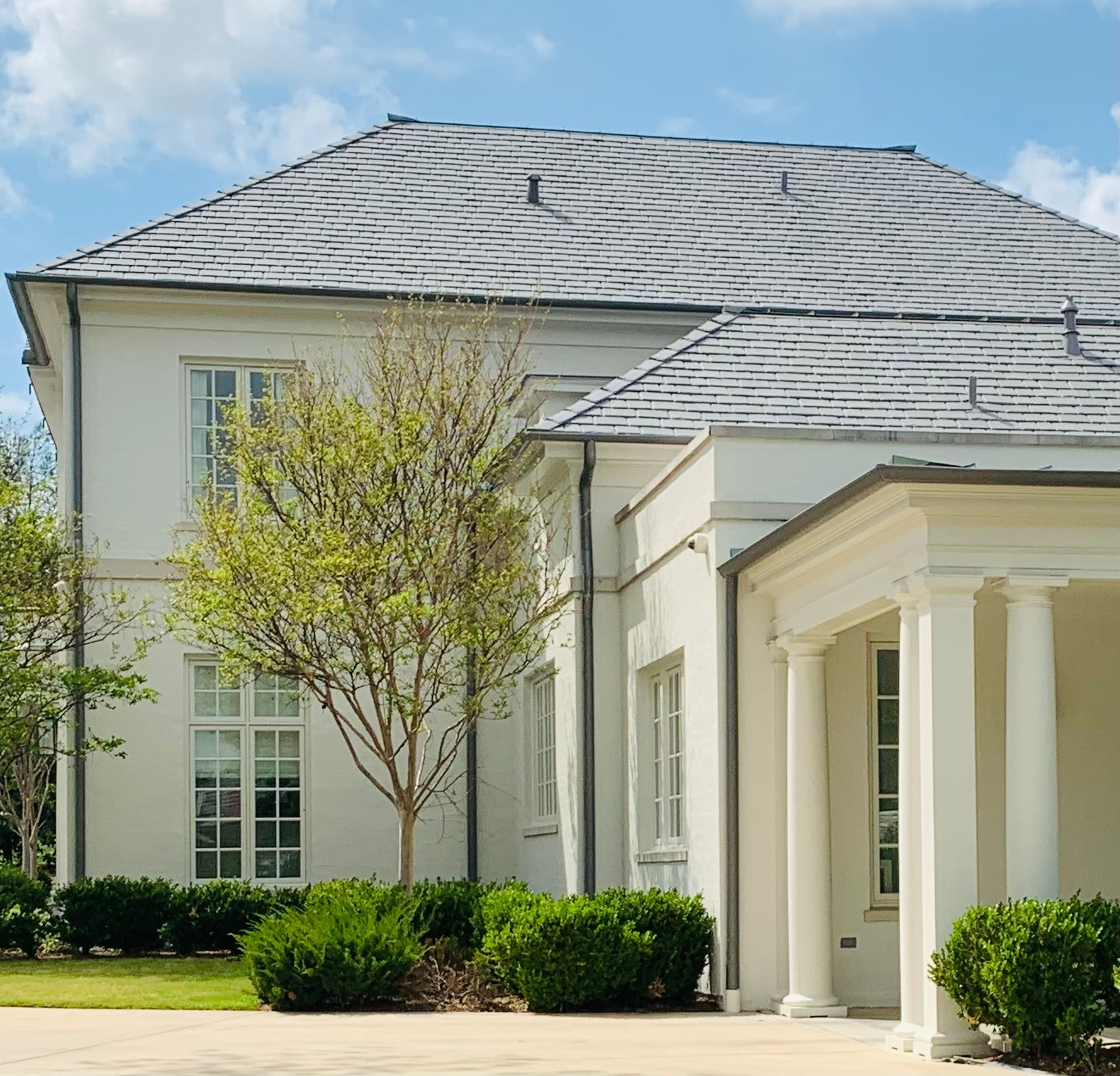 White mansion with gray tiled roof, columns, and a tree in front.