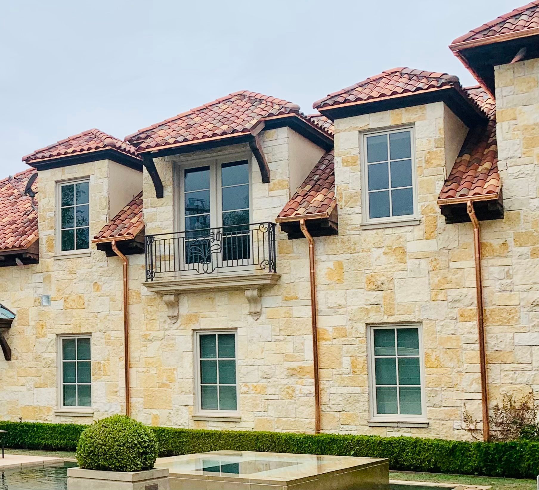 Stone building with red-tiled roof, multiple windows, and a small balcony. Cloudy sky.