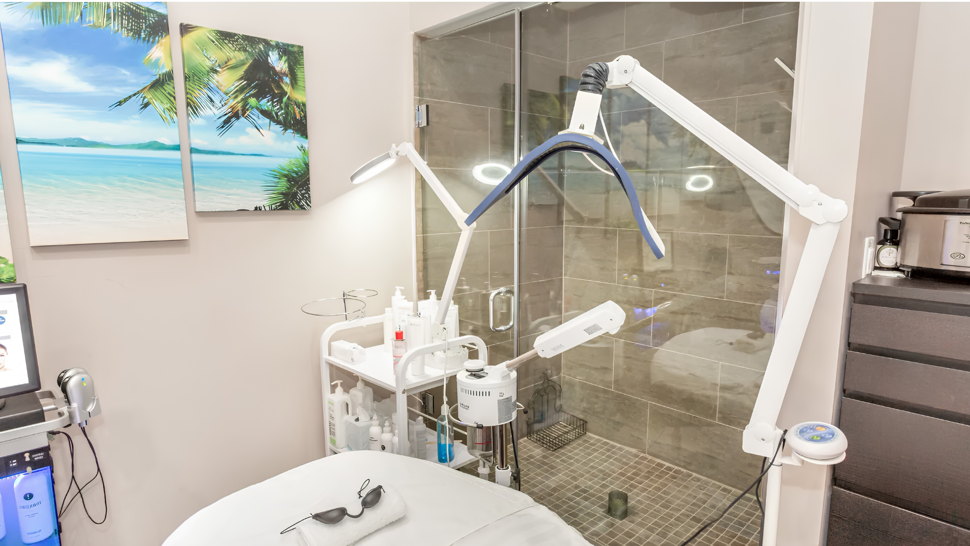 Dental clinic room with chair, overhead light, and equipment beside a beach wall art and gray cabinet
