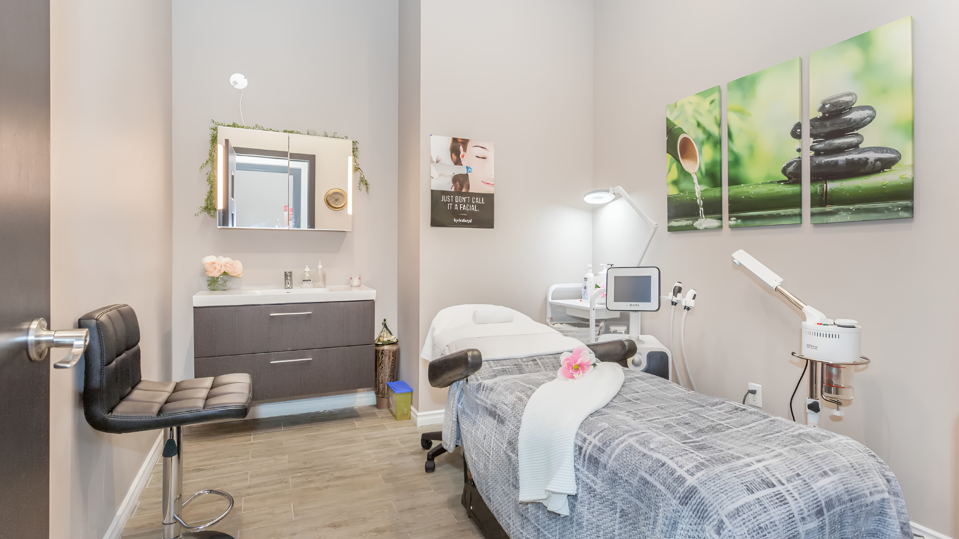 Modern treatment room with an exam table, medical equipment, and wall art in soft neutral tones