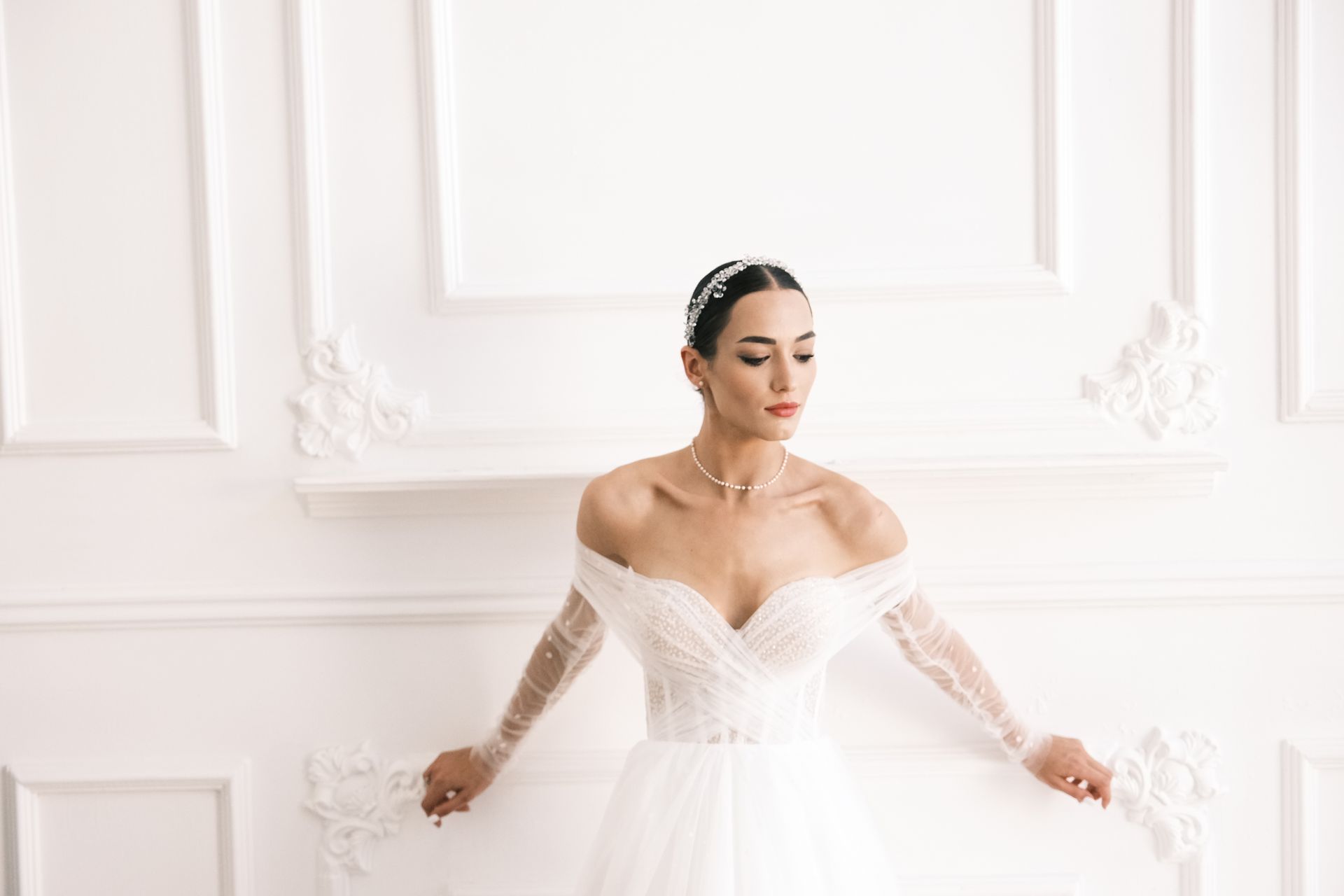 Bride in a white off-shoulder gown standing in a bright, elegant room