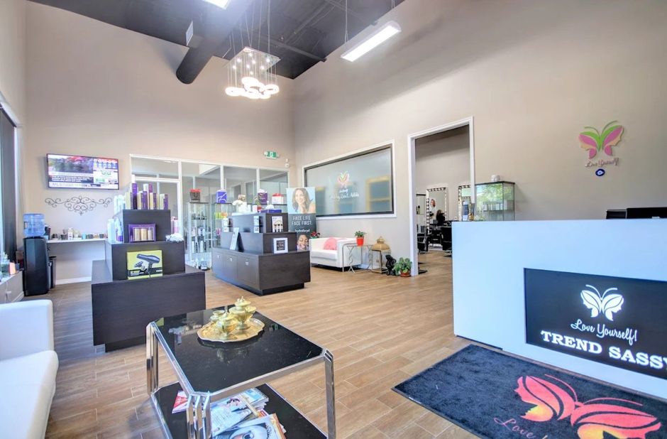 Modern salon lobby with white counter, black chairs, product displays, and a TV on the right