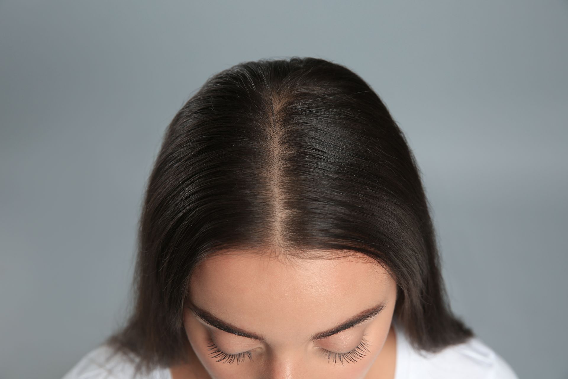 Person with dark hair looking downward against a gray background