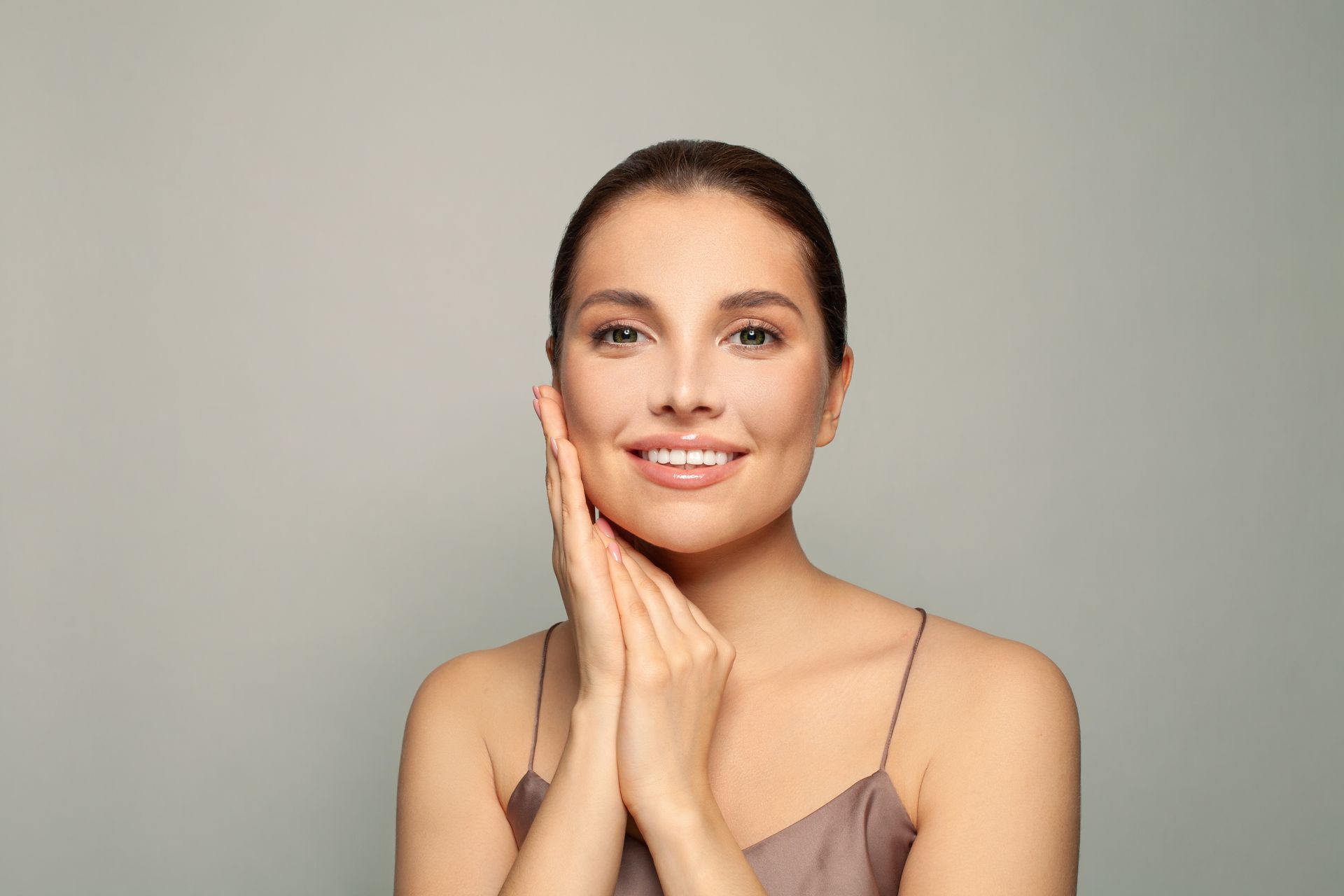 Smiling woman with hands on her cheeks against a plain gray background