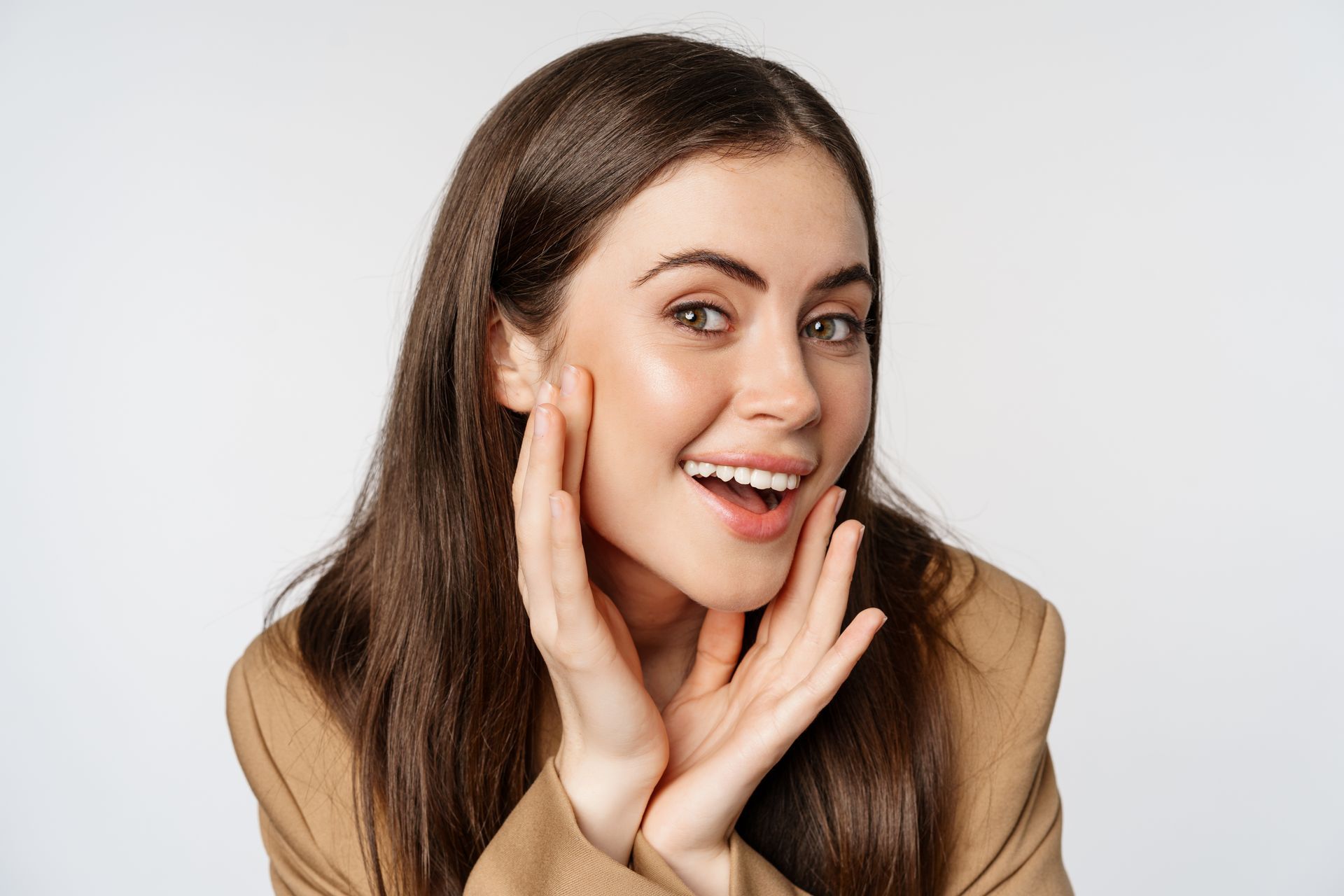 Smiling woman with long dark hair holding her hands near her face against a white background