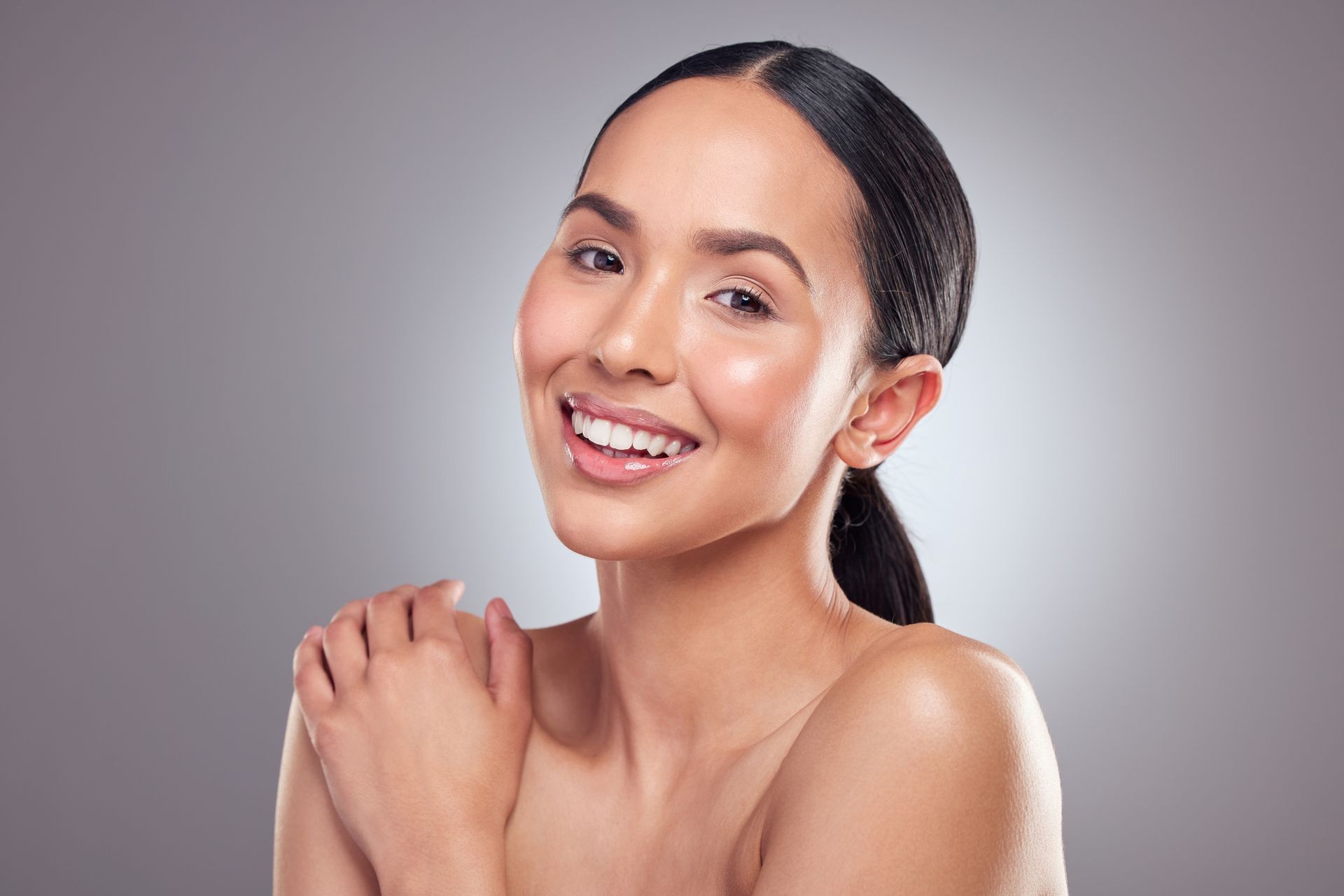Smiling person with bare shoulders against a soft gray background