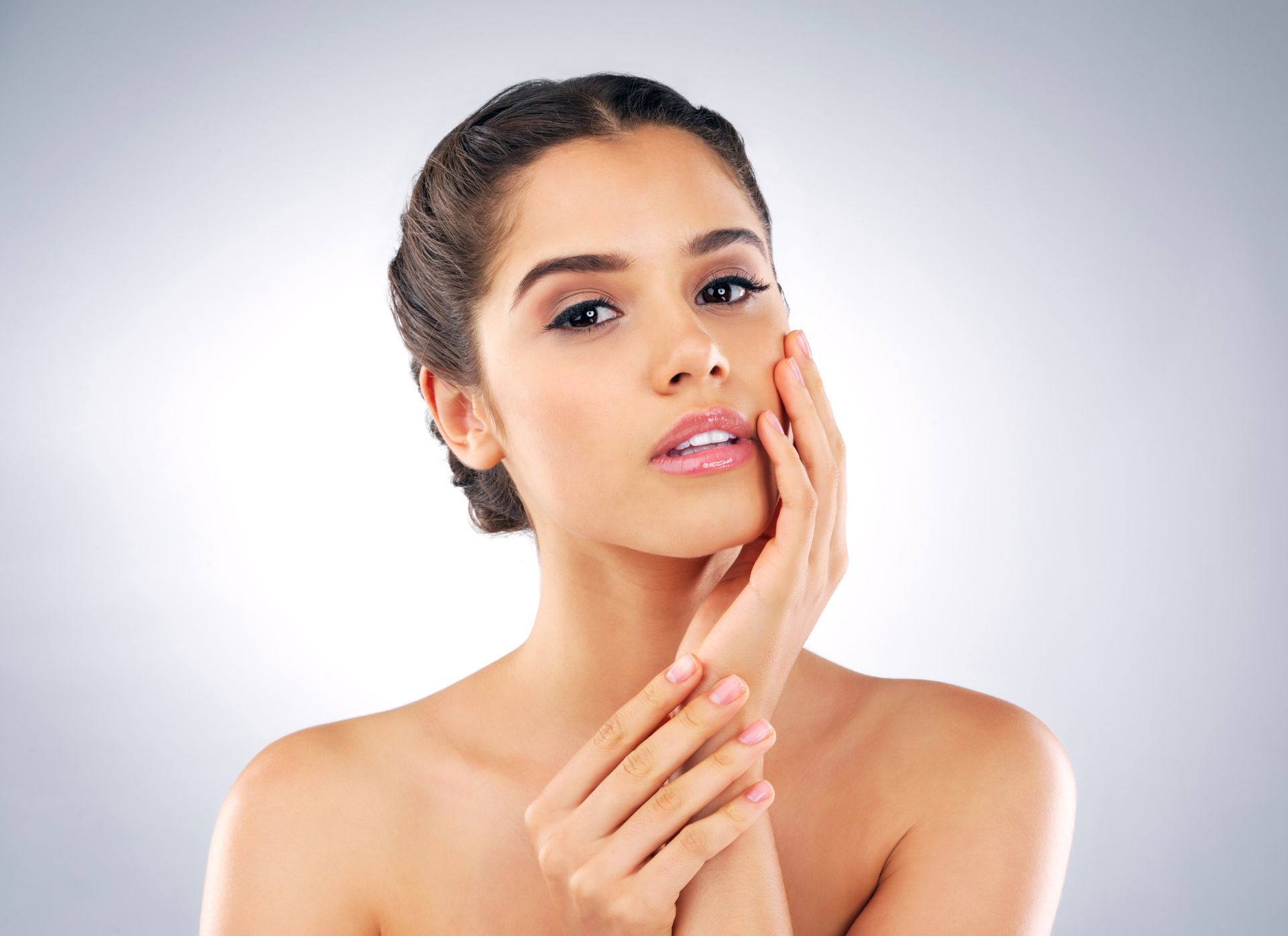Woman gently applying skincare cream to her face against a light gray background