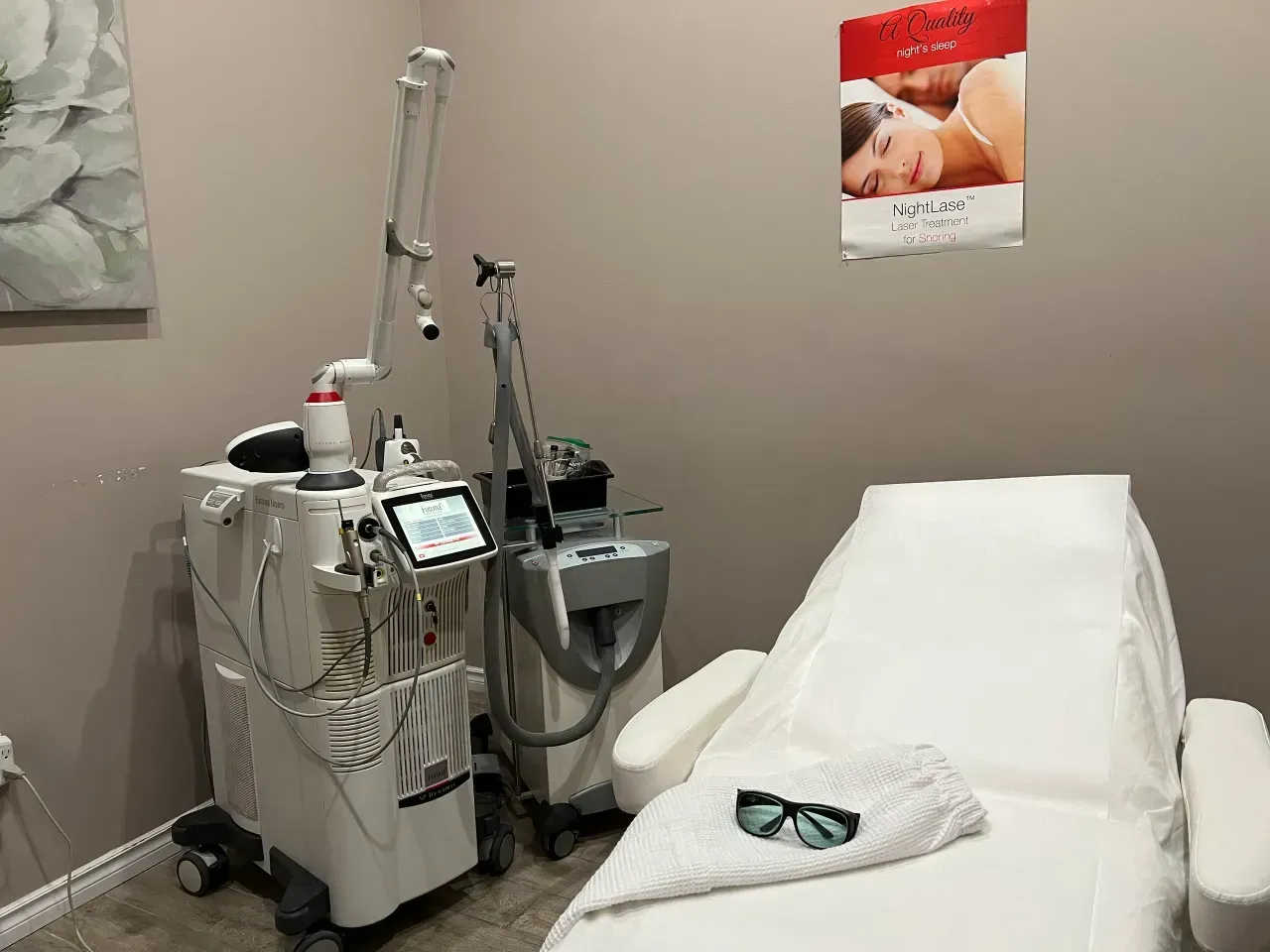 Medical treatment room with a reclining exam chair, laser equipment, and protective goggles on a towel.