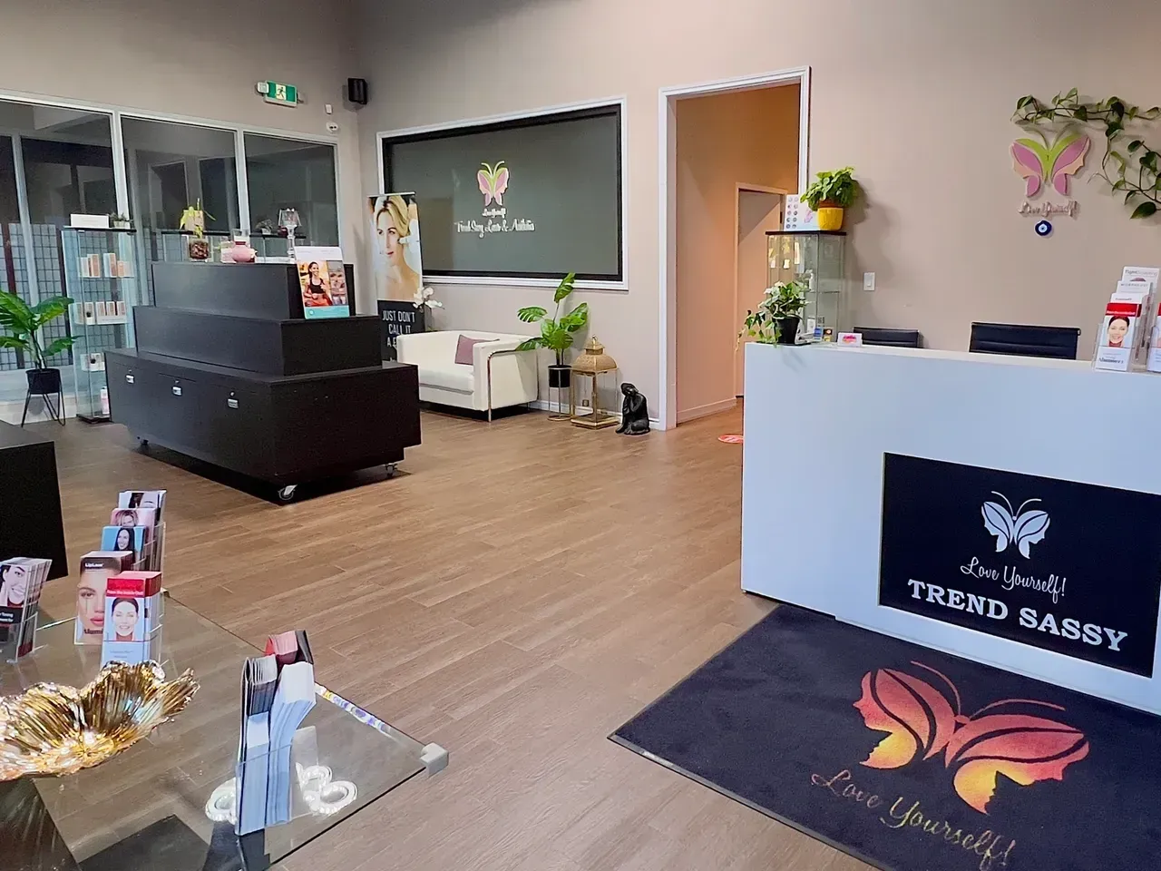Bright modern salon lobby with white reception desk, black sofa, plants, and wood floor in soft pink decor