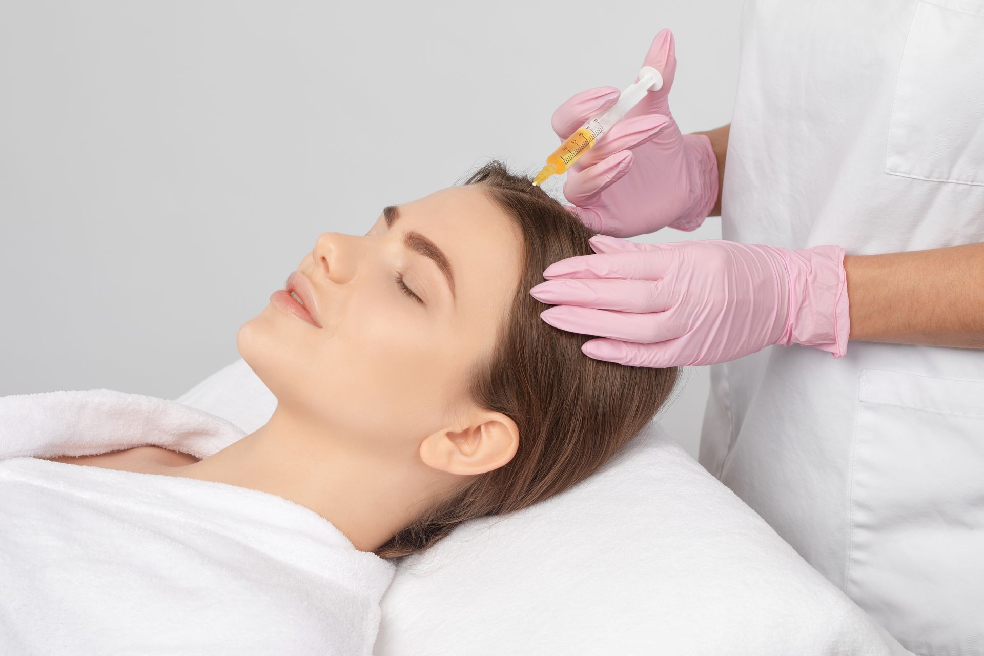 Cosmetic injection treatment on a woman lying on a spa bed, with gloved hands preparing her hairline