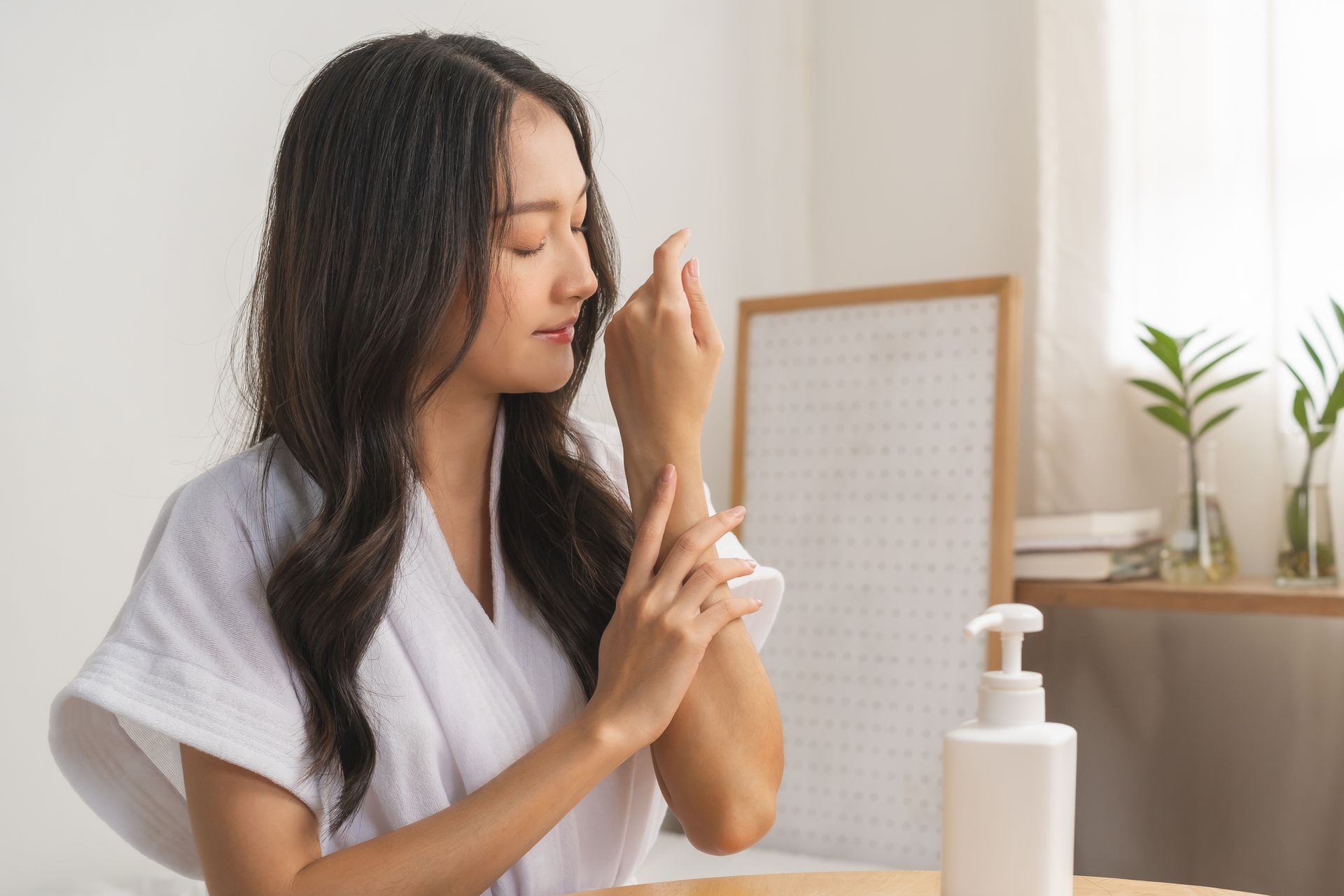 Woman applying lotion to her face at a table beside a white pump bottle
