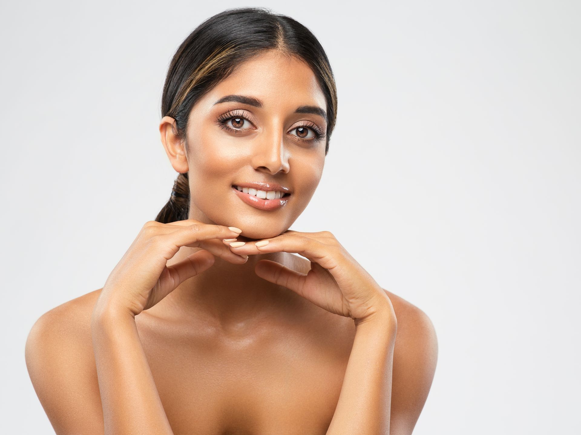Portrait of a smiling person resting their chin on clasped hands against a light gray background