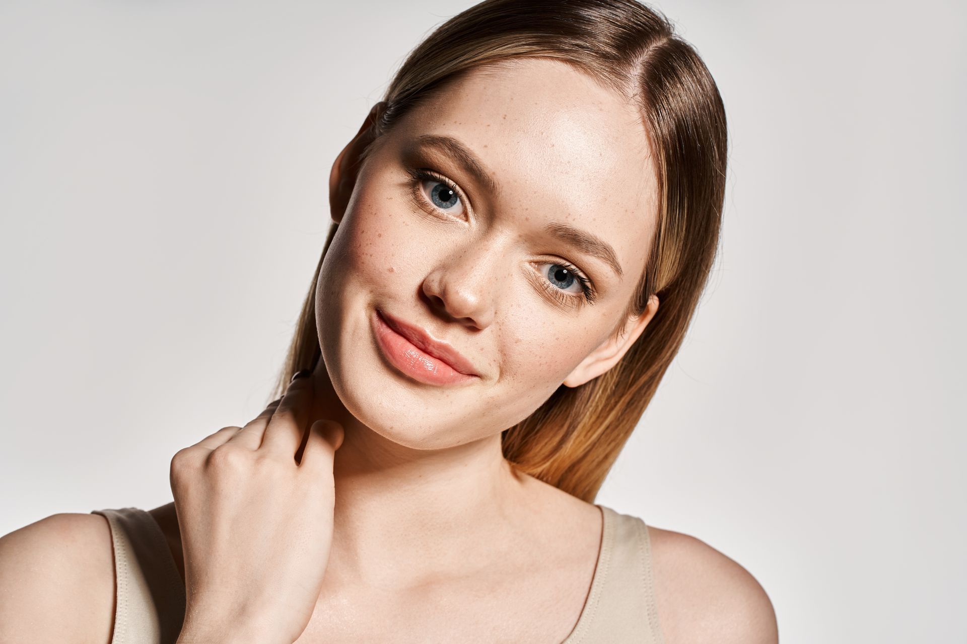 Close-up portrait of a smiling woman with hand on shoulder against a light background
