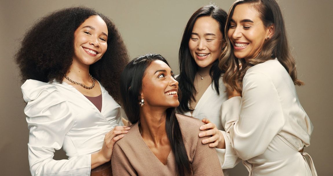 Four smiling people in light outfits posing closely together against a neutral background.