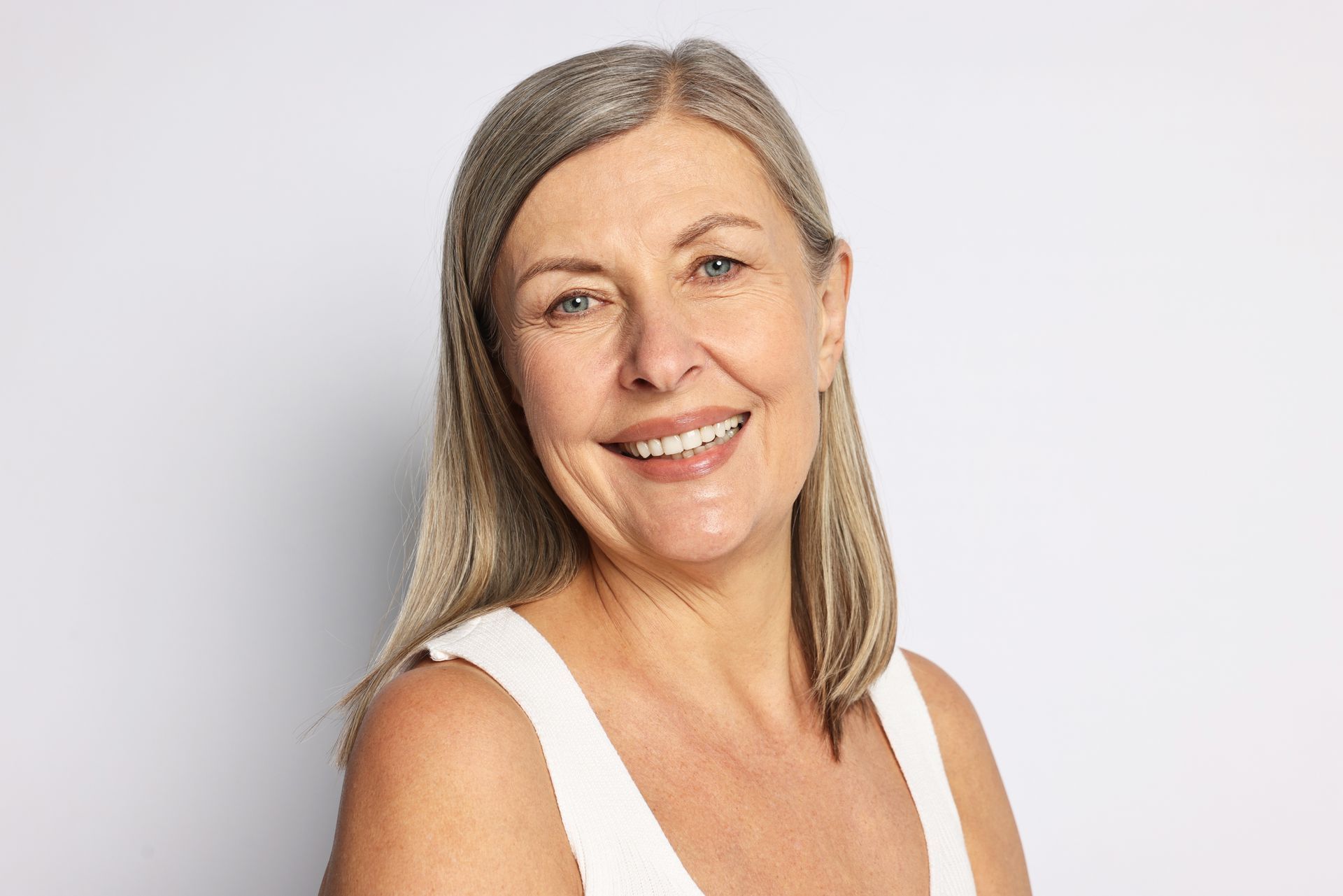 Smiling woman with gray hair in a white top against a light background