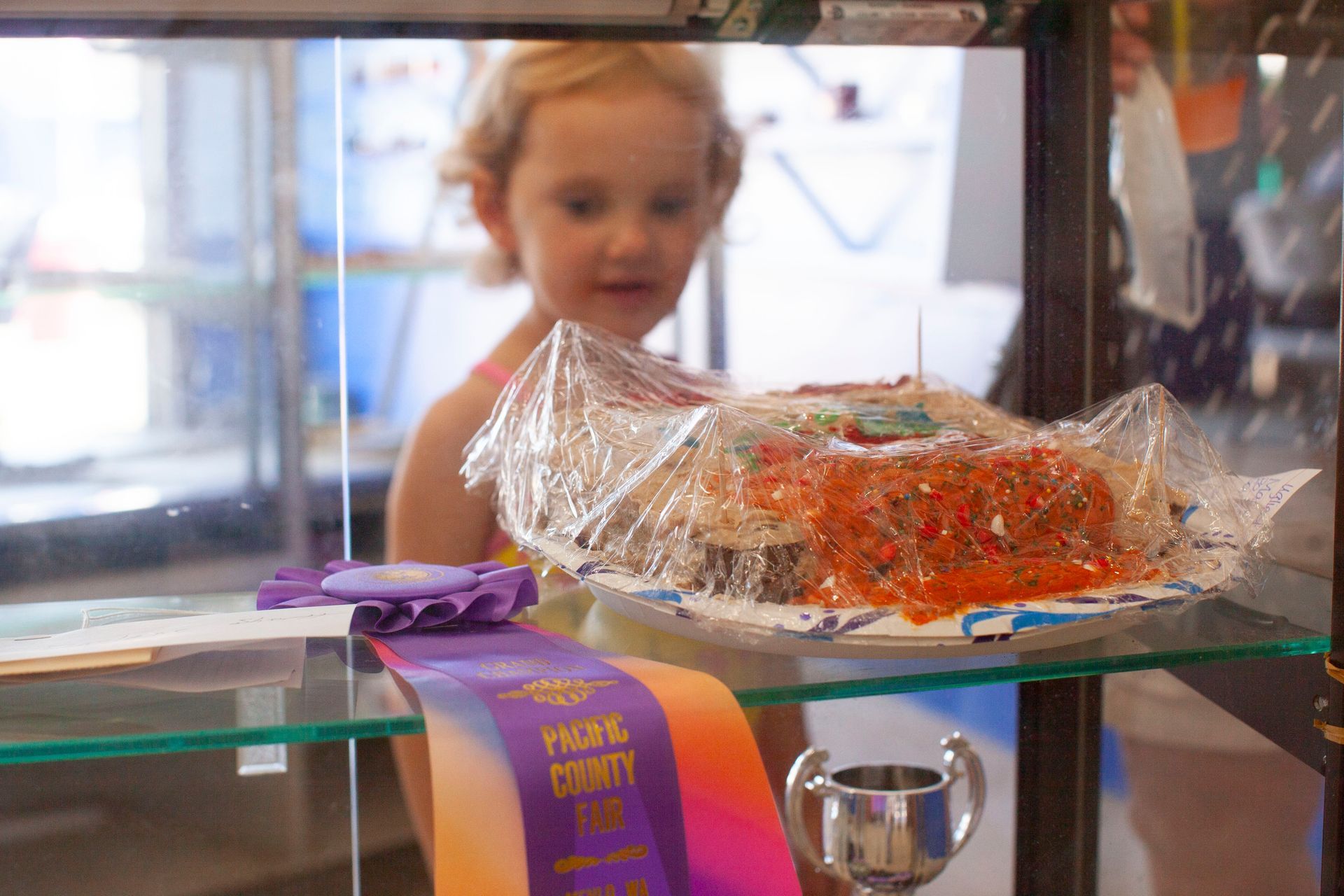 A little girl is looking at a cake in a display case
