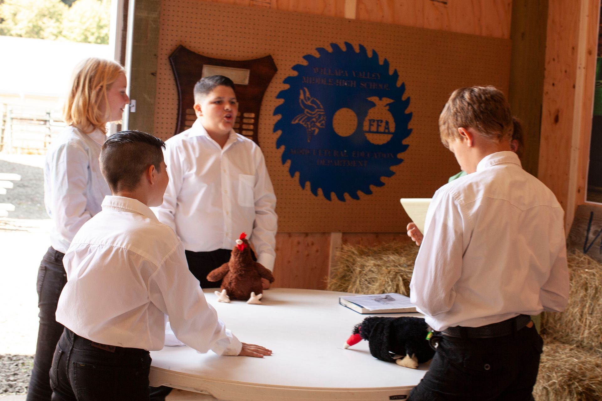 A group of young people are standing around a table with a circular saw blade in the background.