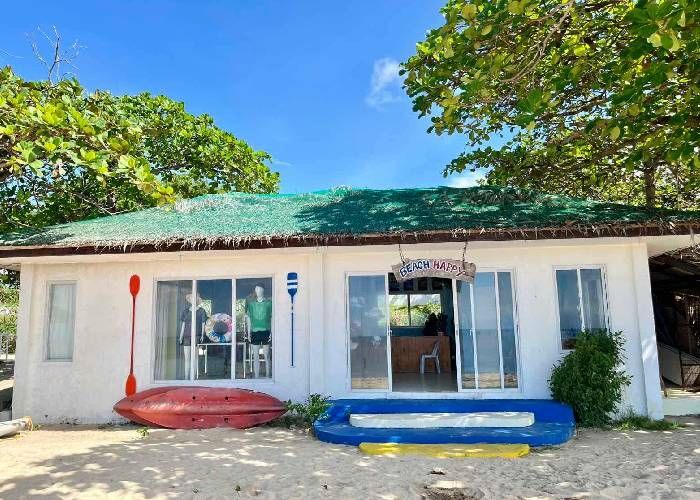White beachside building with kayaks, paddles, and open doorway, blue sky.