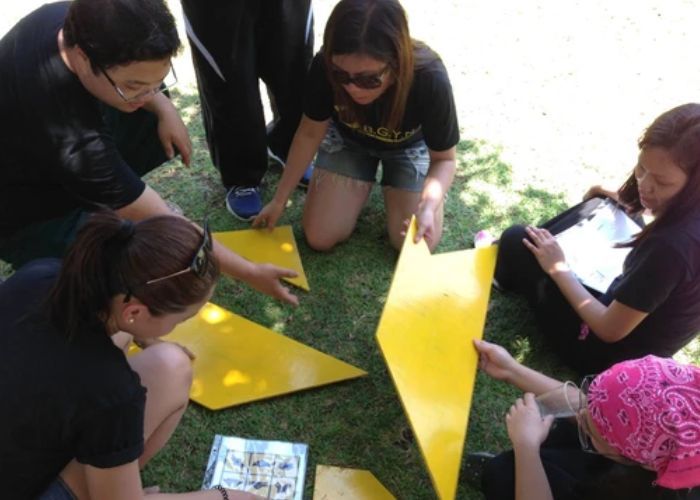 Group of people assembling yellow shapes on grass outdoors.