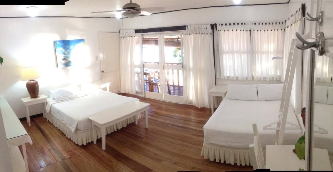 Bright bedroom with two beds, white linens, balcony access, hardwood floors.