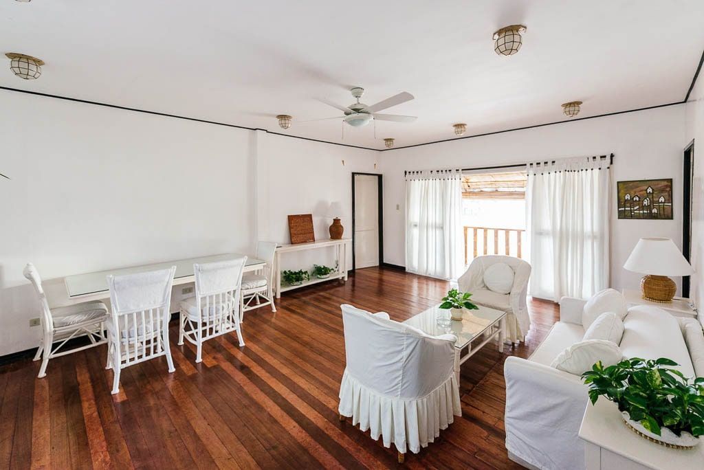 Spacious, bright living room with white furniture, wooden floors, and a balcony.