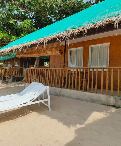 Beachside bungalow with green roof, bamboo railing and beach chair on the sand.
