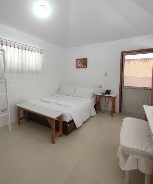 White-walled hotel room with a bed, bench, small table, and doorway.