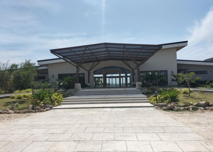 Stone path leading to a modern building with a canopy entrance and glass doors under a blue sky.